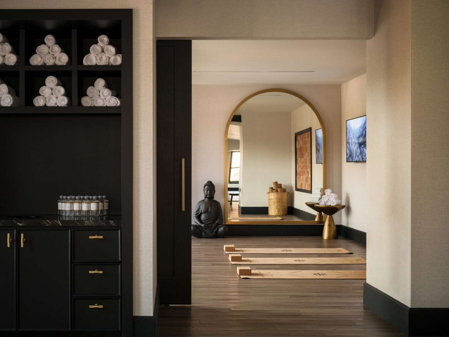 Modern yoga room, with dark shelves filled with towels, yoga mats with blocks on the floor, large arched mirror on back wall