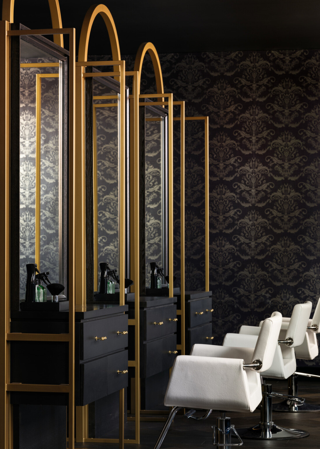 Luxurious hotel salon filled with black and gold furniture along the walls and a series of white salon chairs in the middle of the room. Black and gold wallpaper line the walls