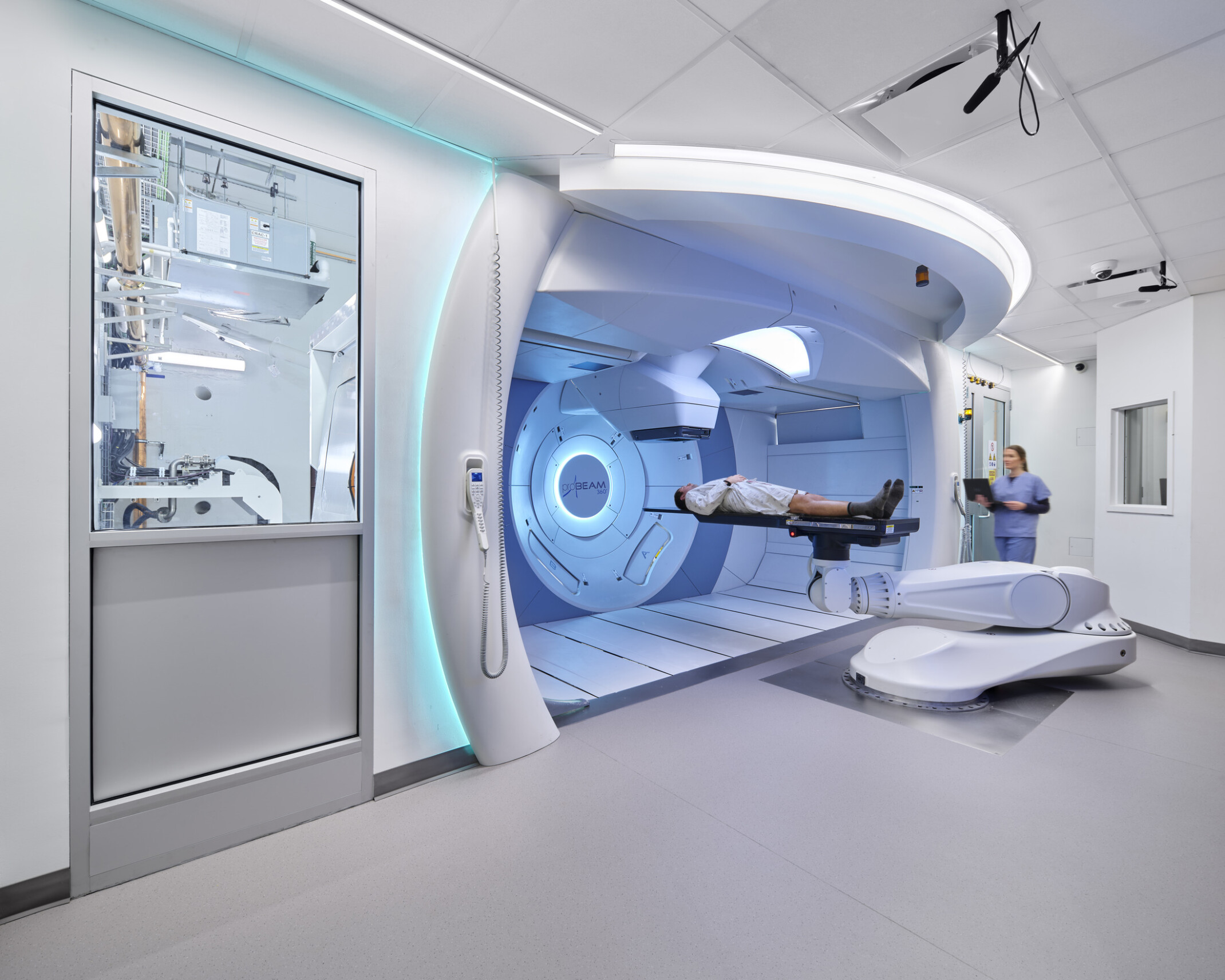 Modern medical facility with a patient on a robotic treatment table in front of a large circular machine, assisted by a medical professional.