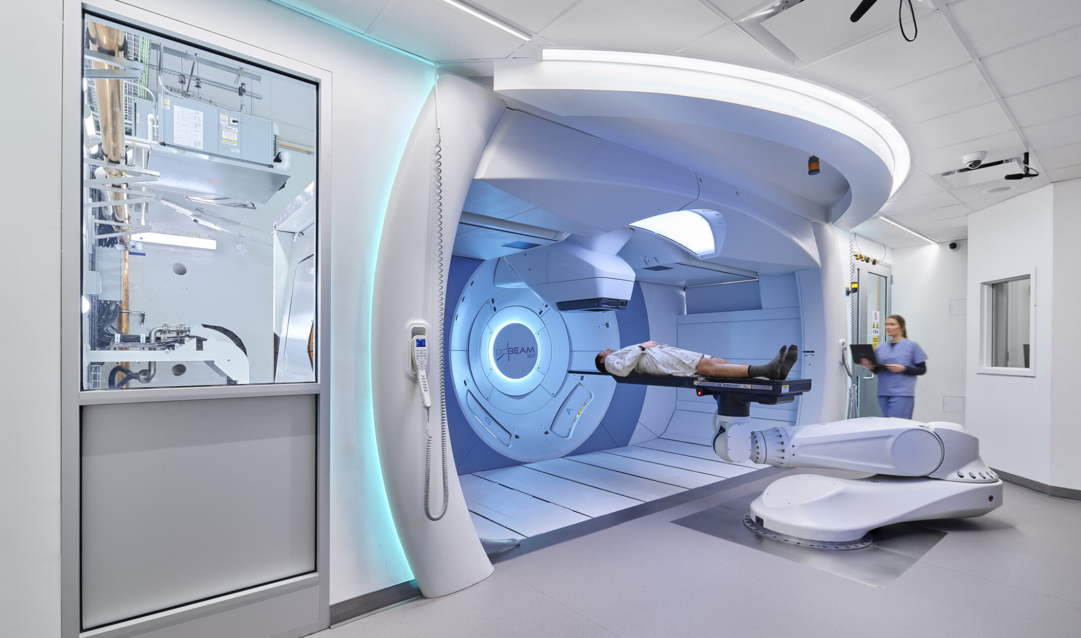 Modern medical facility with a patient on a robotic treatment table in front of a large circular machine, assisted by a medical professional.