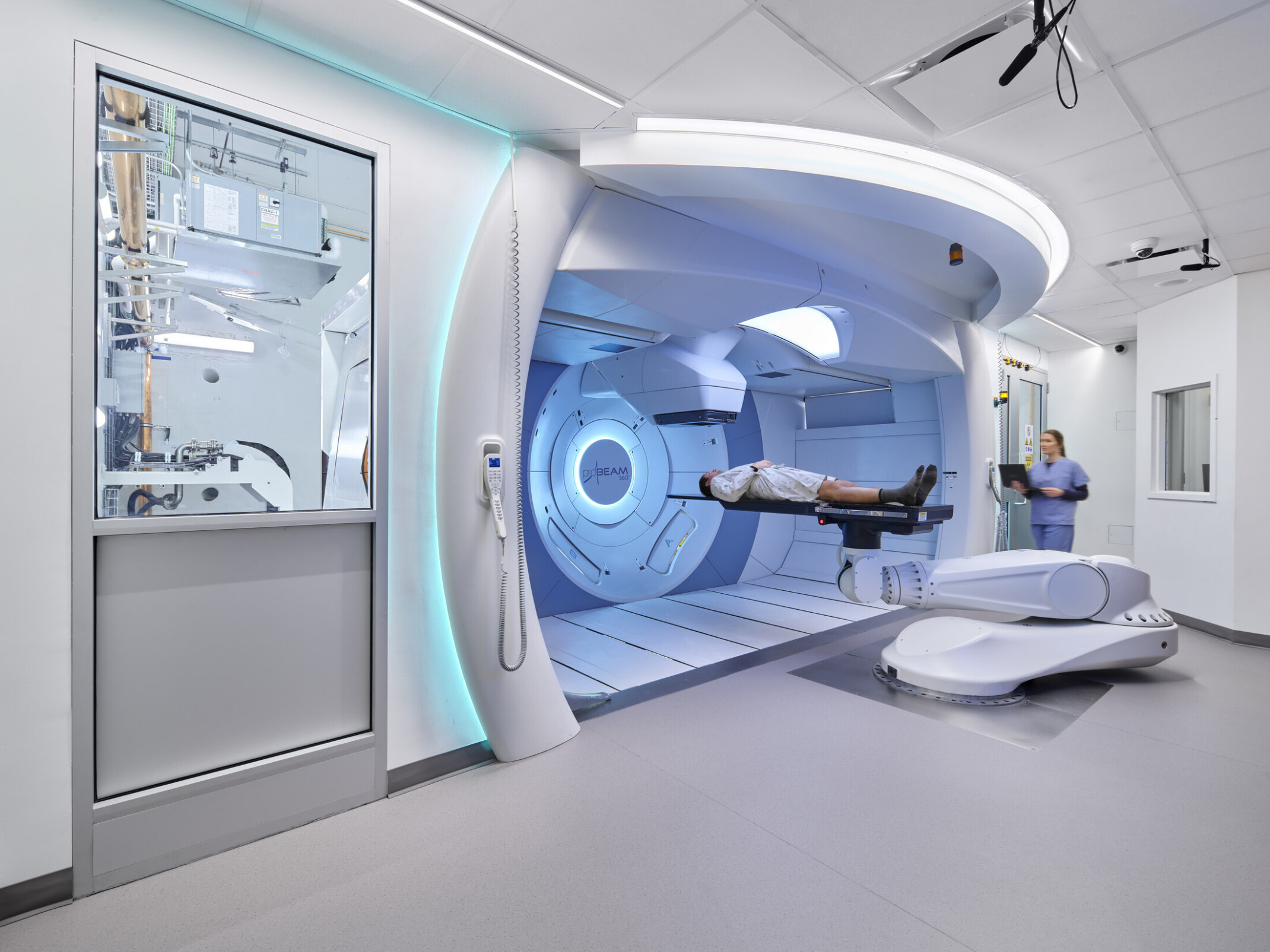 Modern medical facility with a patient on a robotic treatment table in front of a large circular machine, assisted by a medical professional.