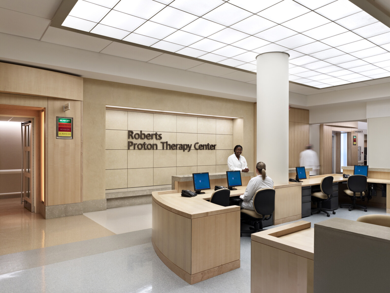 Medical reception area with modern wood furnishings, desks, computers, and signage on the back wall.
