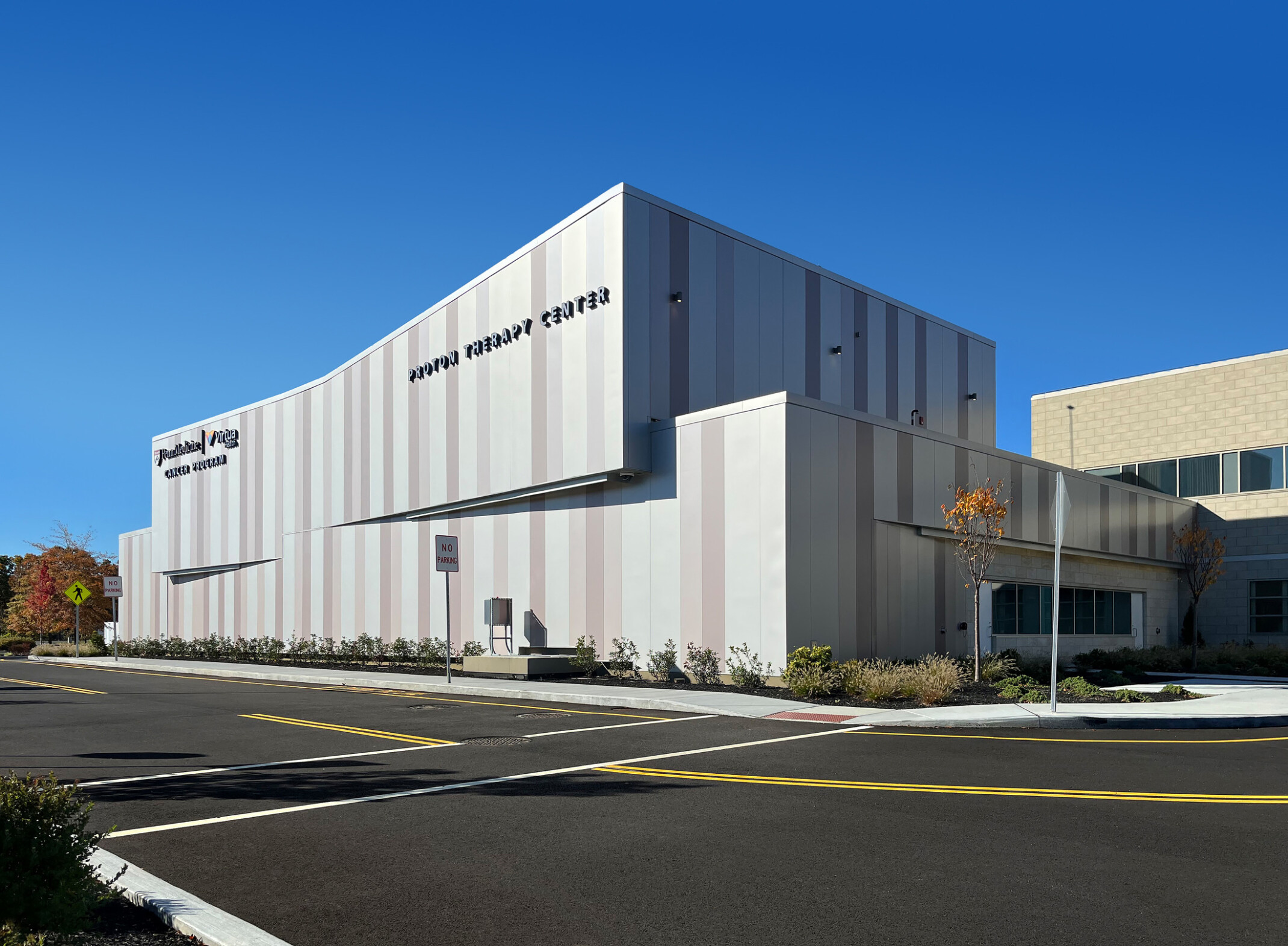 Exterior view of a modern medical facility. The building features a sleek design with vertical panels in soft beige and white tones, set against a clear blue sky.