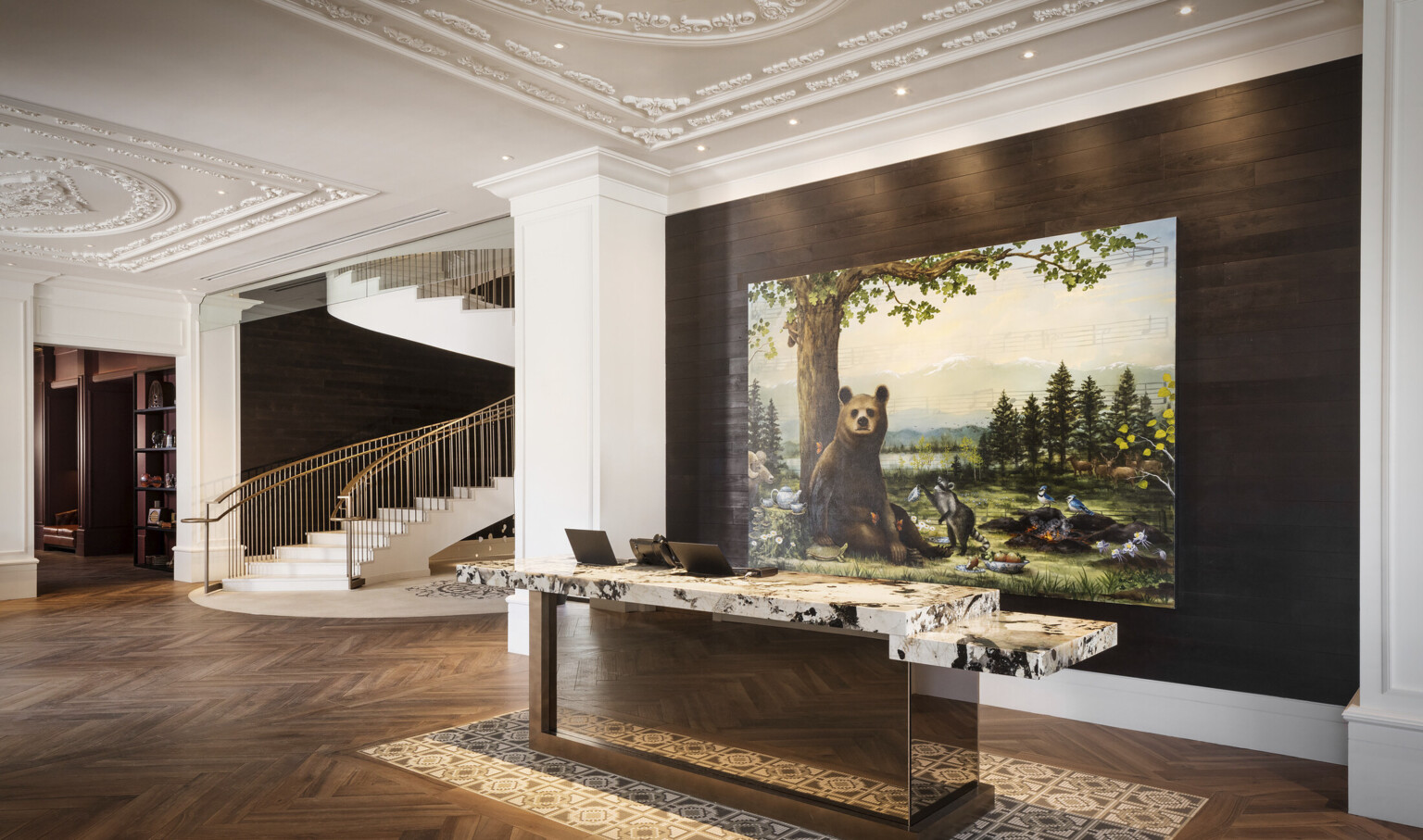 Reception desk with white and black marble counter in white lobby in front of recessed wood wall with painting of a bear