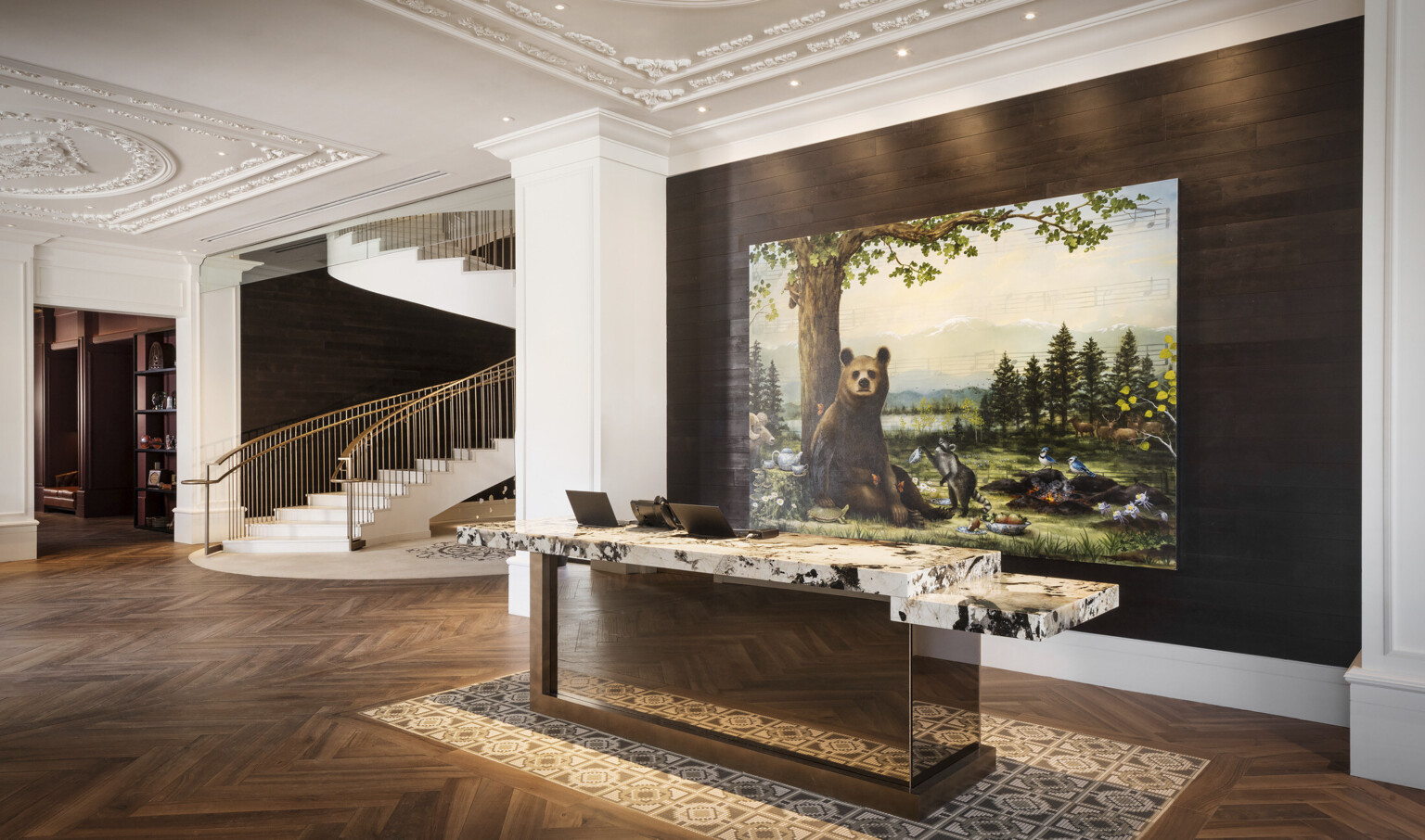 Reception desk with white and black marble counter in white lobby in front of recessed wood wall with painting of a bear
