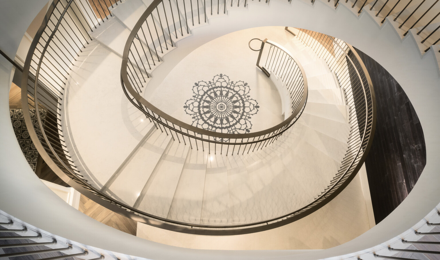 View from above of white spiral staircase with metallic railing. At the center of the floor in the spiral is a black mandala
