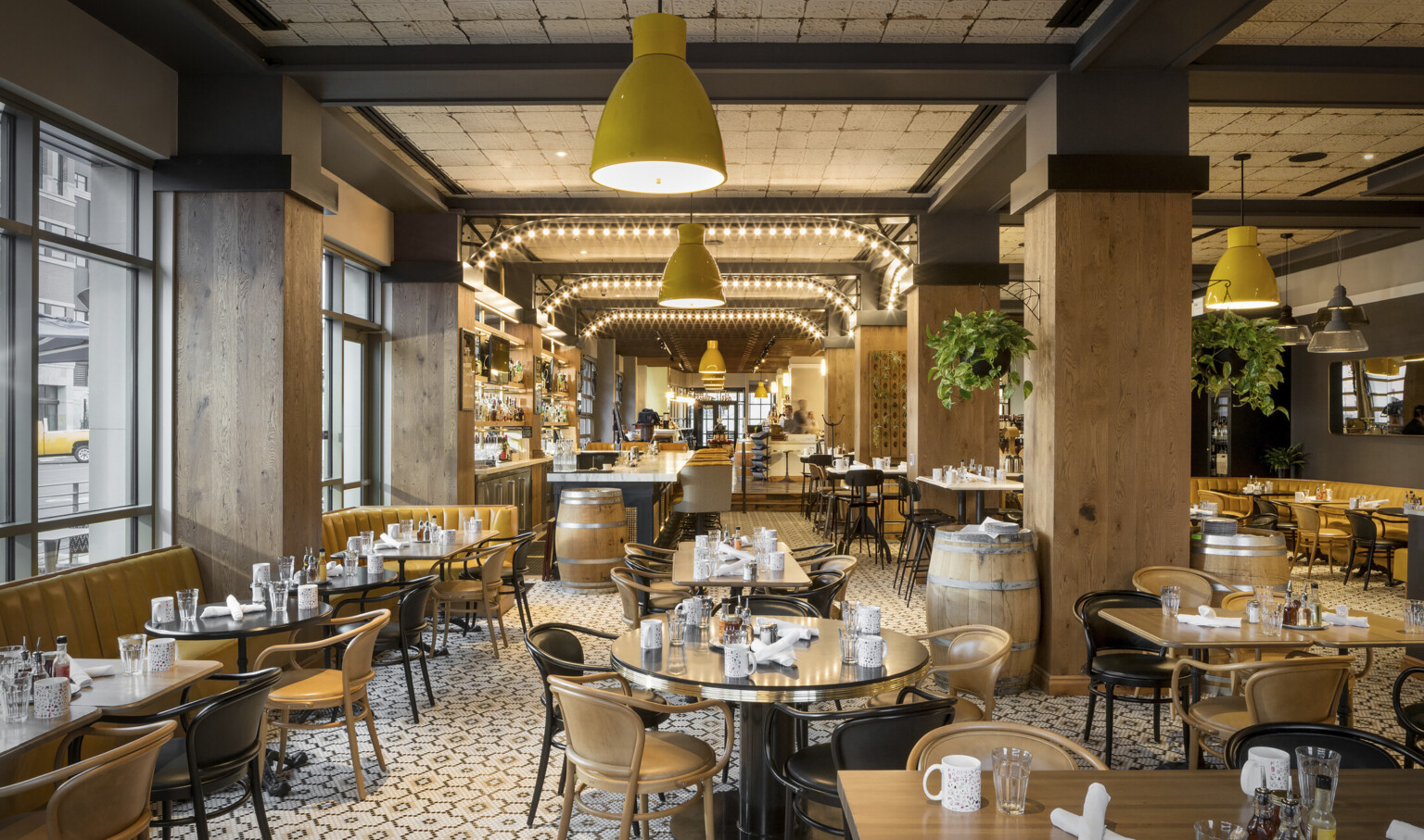 Dining area with illuminated metal archways between wood pillars. Yellow booths along left wall and neutral toned seating