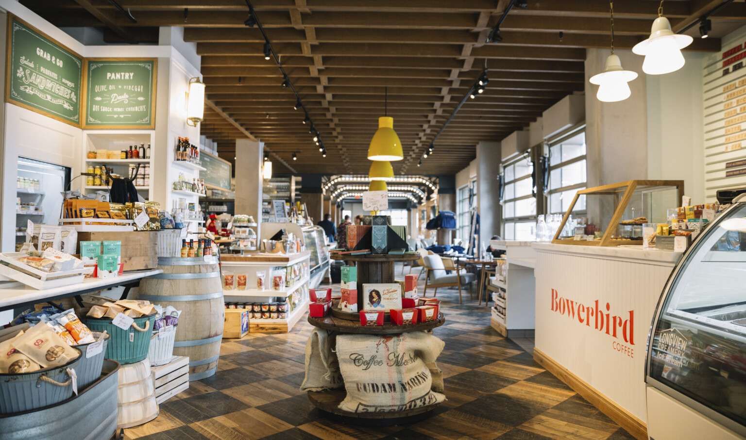Round wood display with candy in a shop next to white counter with Bowerbird Coffee sign to right. Wood floor and ceiling