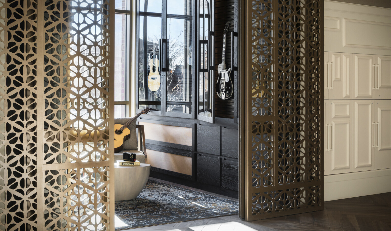 Organic shaped translucent metallic doorframe wraps around opening to room with black, glass door cabinet holding guitars