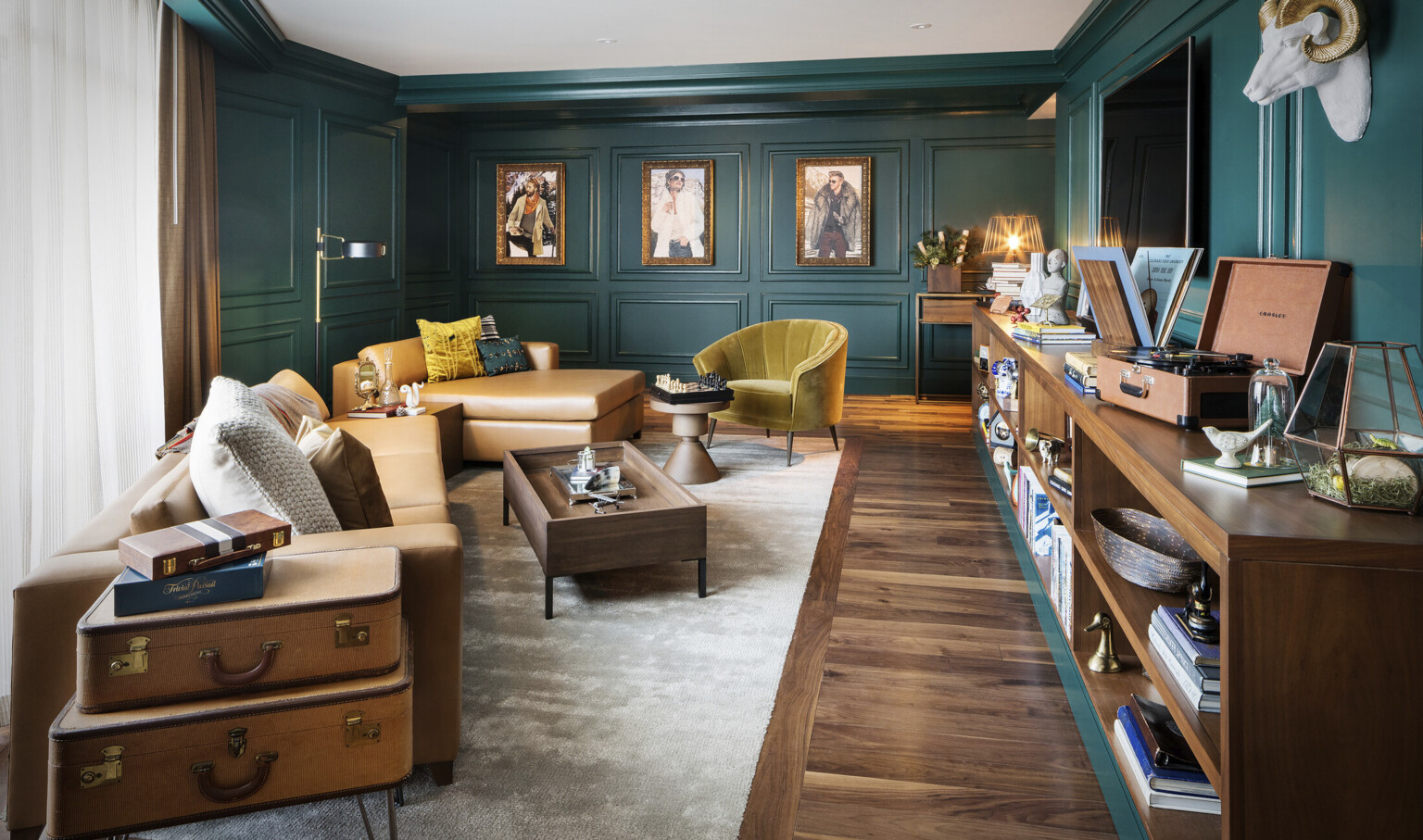 Sitting room with dark green molded walls. Light brown leather couch and yellow velvet chair with wood coffee table and shelf