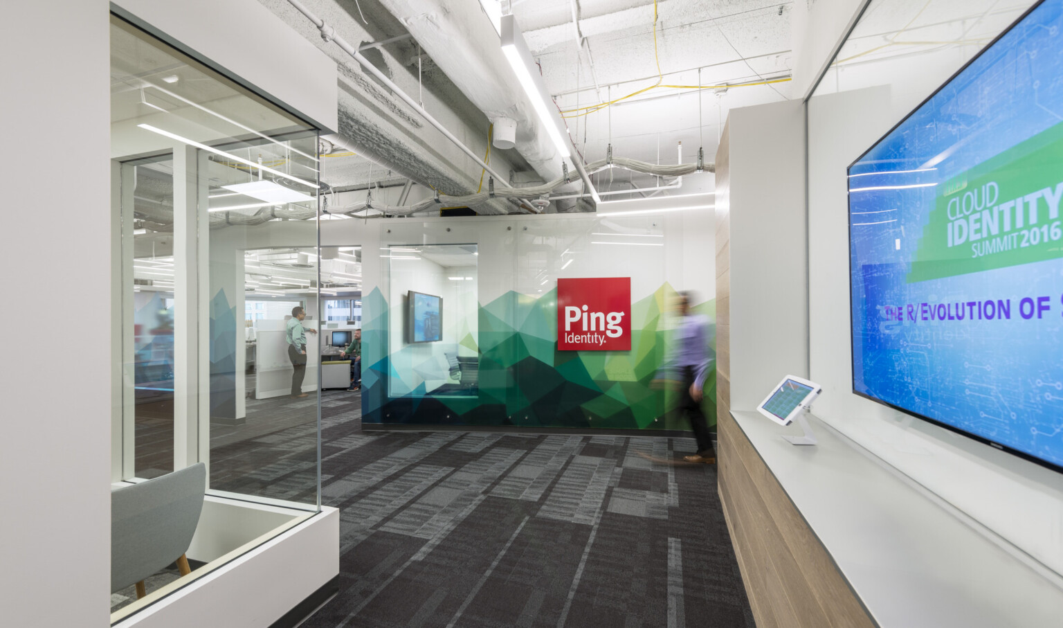 Hallway facing sign for Ping Identity on white wall with angular abstract green and blue mural along base Hallway facing sign for Ping Identity on white wall with angular abstract green and blue mural along base