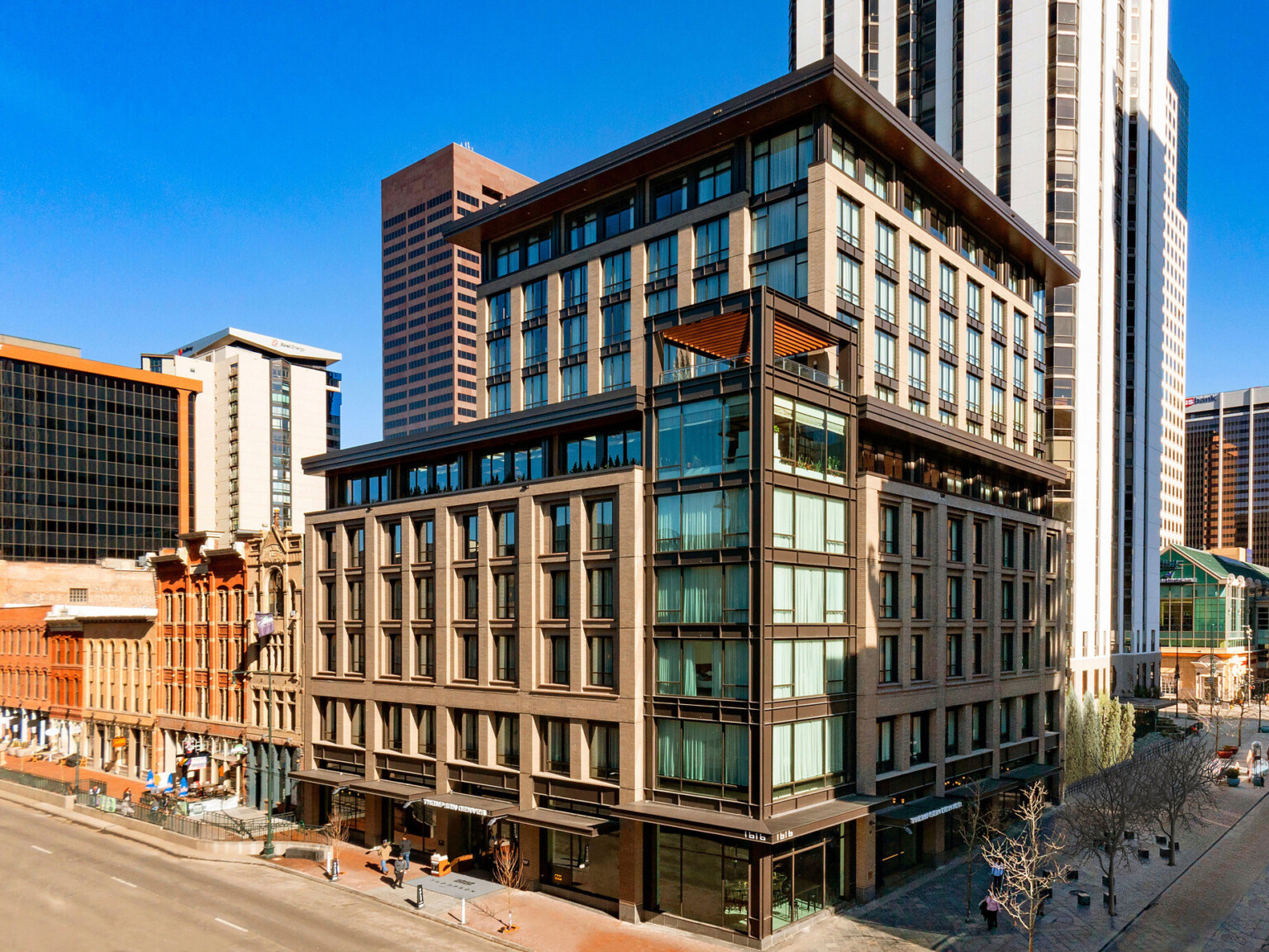 The Thompson Hotel Denver seen from corner with glass tower and stone façade on each side.