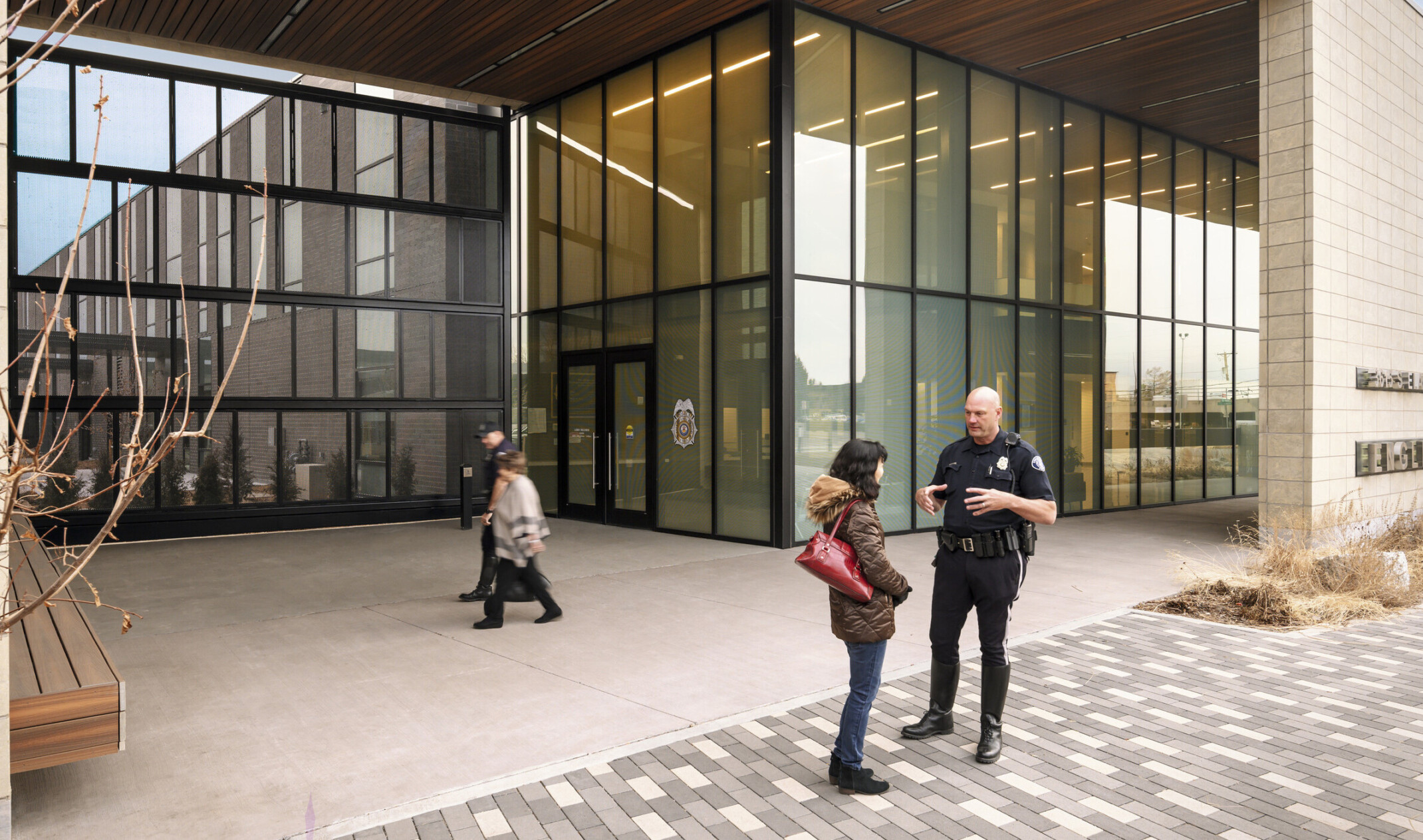 Police officer speaks with woman outside double height glass canopied entrance to Englewood Police Headquarters
