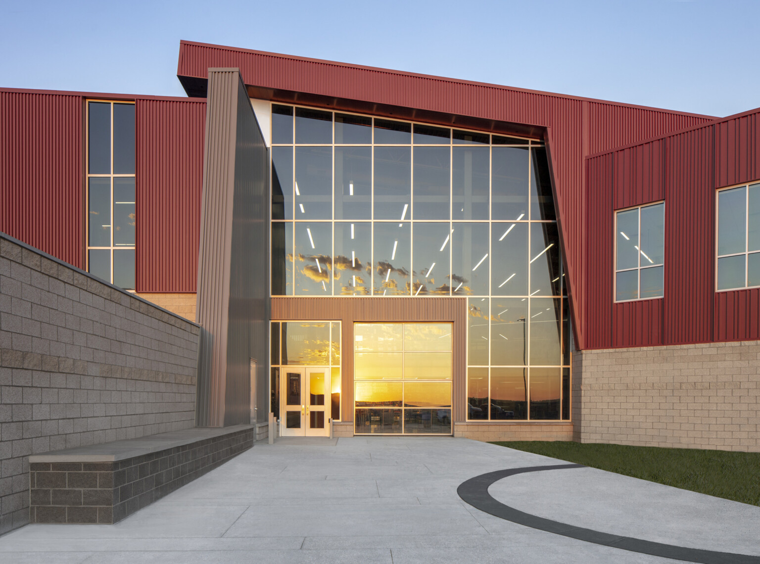 front entrance to a building; nonsymmetrical building construction which is red and gray stone; sunset reflecting the floor to ceiling windows of the entrance