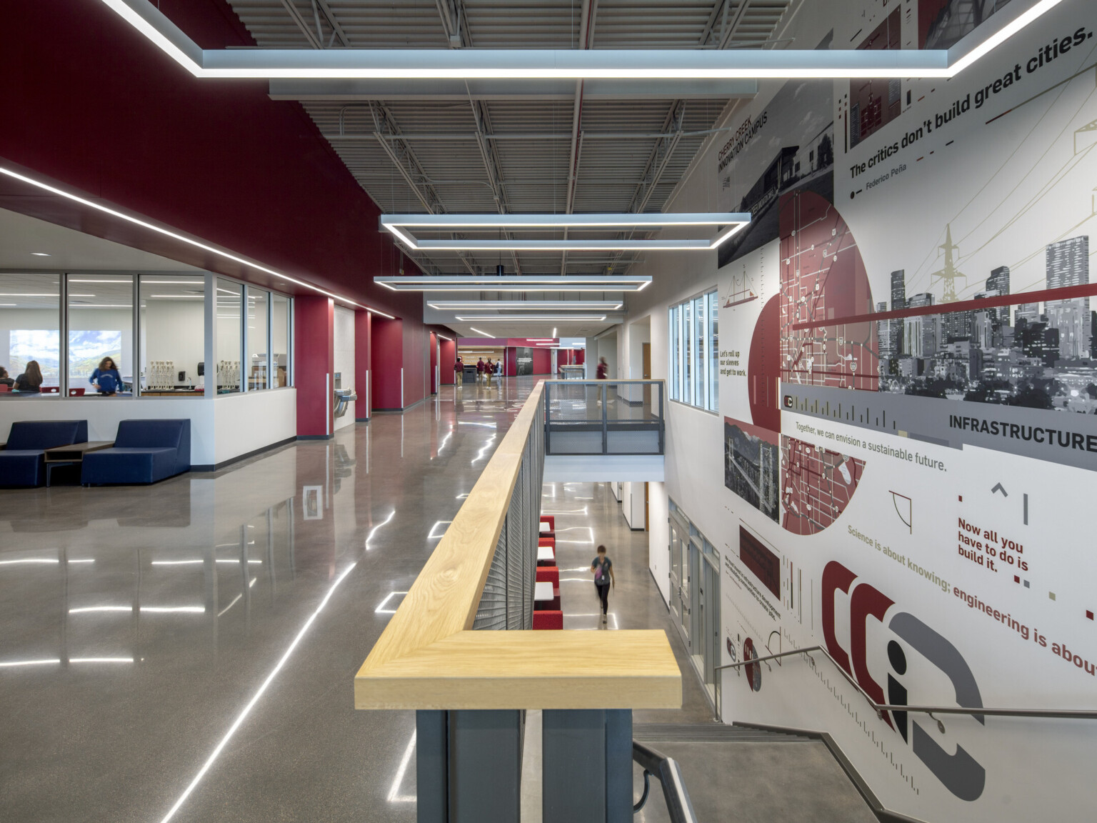 Mural on right wall next to stairs to 2nd floor. Red wall to left with white recession with seating by classroom windows