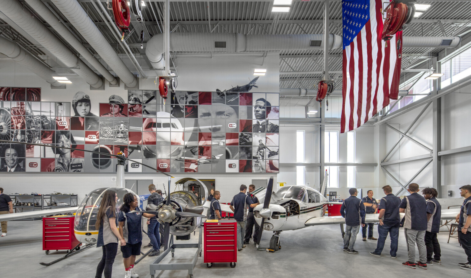 Aviation lab with helicopter, small plane, and displayed engine, mural at back with planes and pilots, american flag, right Aviation lab with helicopter, small plane, and displayed engine, mural at back with planes and pilots, american flag, right