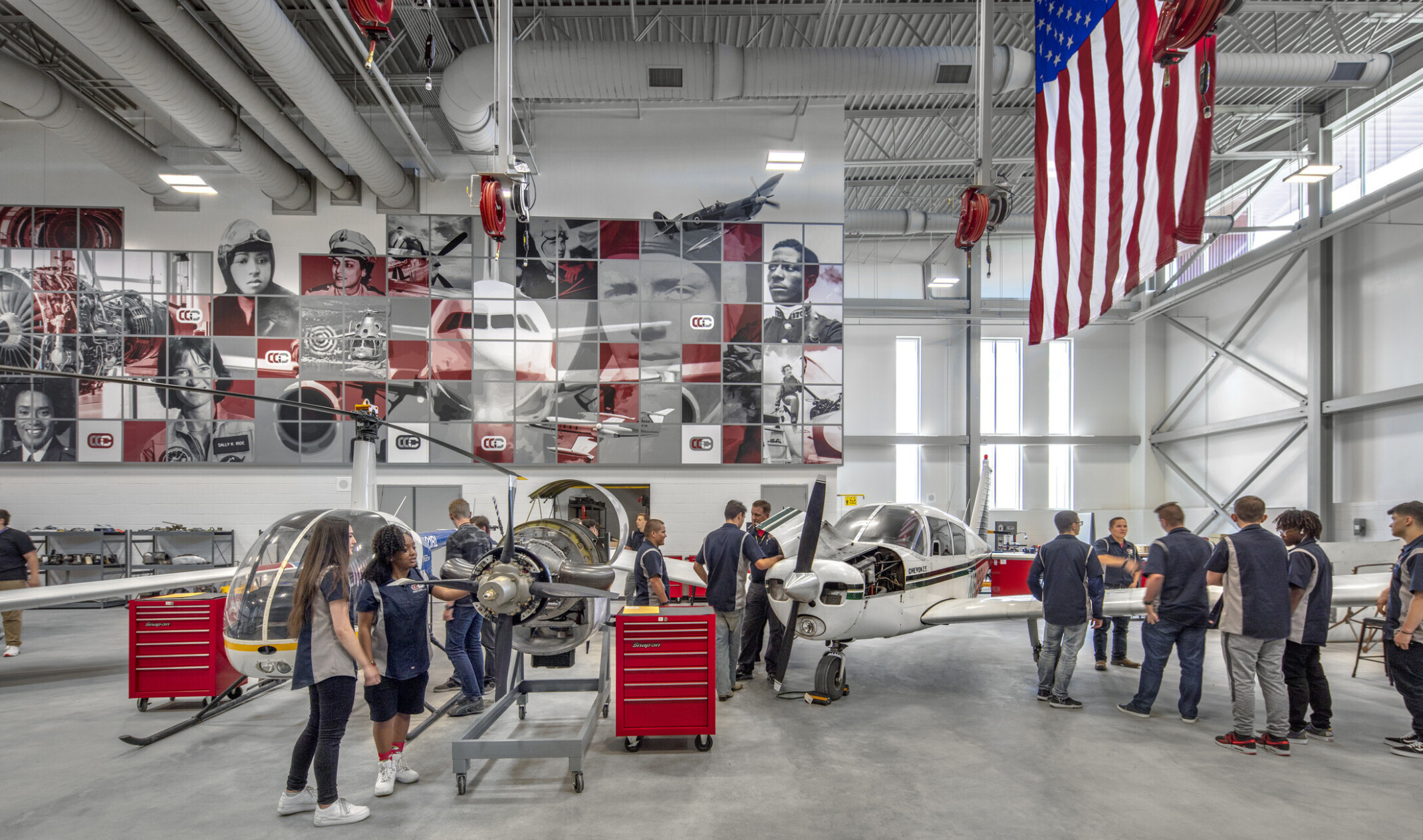 Aviation lab with helicopter, small plane, and displayed engine, mural at back with planes and pilots, american flag, right