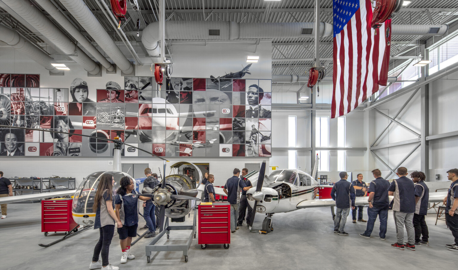 Aviation lab with helicopter, small plane, and displayed engine, mural at back with planes and pilots, american flag, right