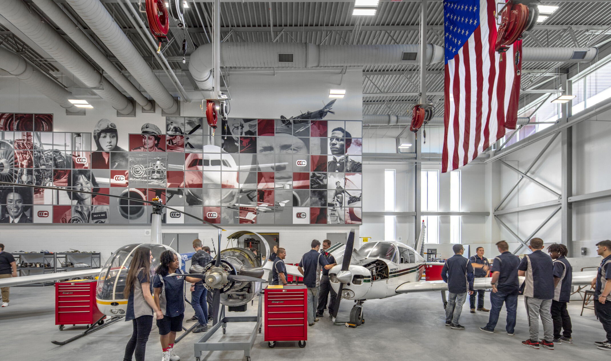 Aviation lab with helicopter, small plane, and displayed engine, mural at back with planes and pilots, american flag, right