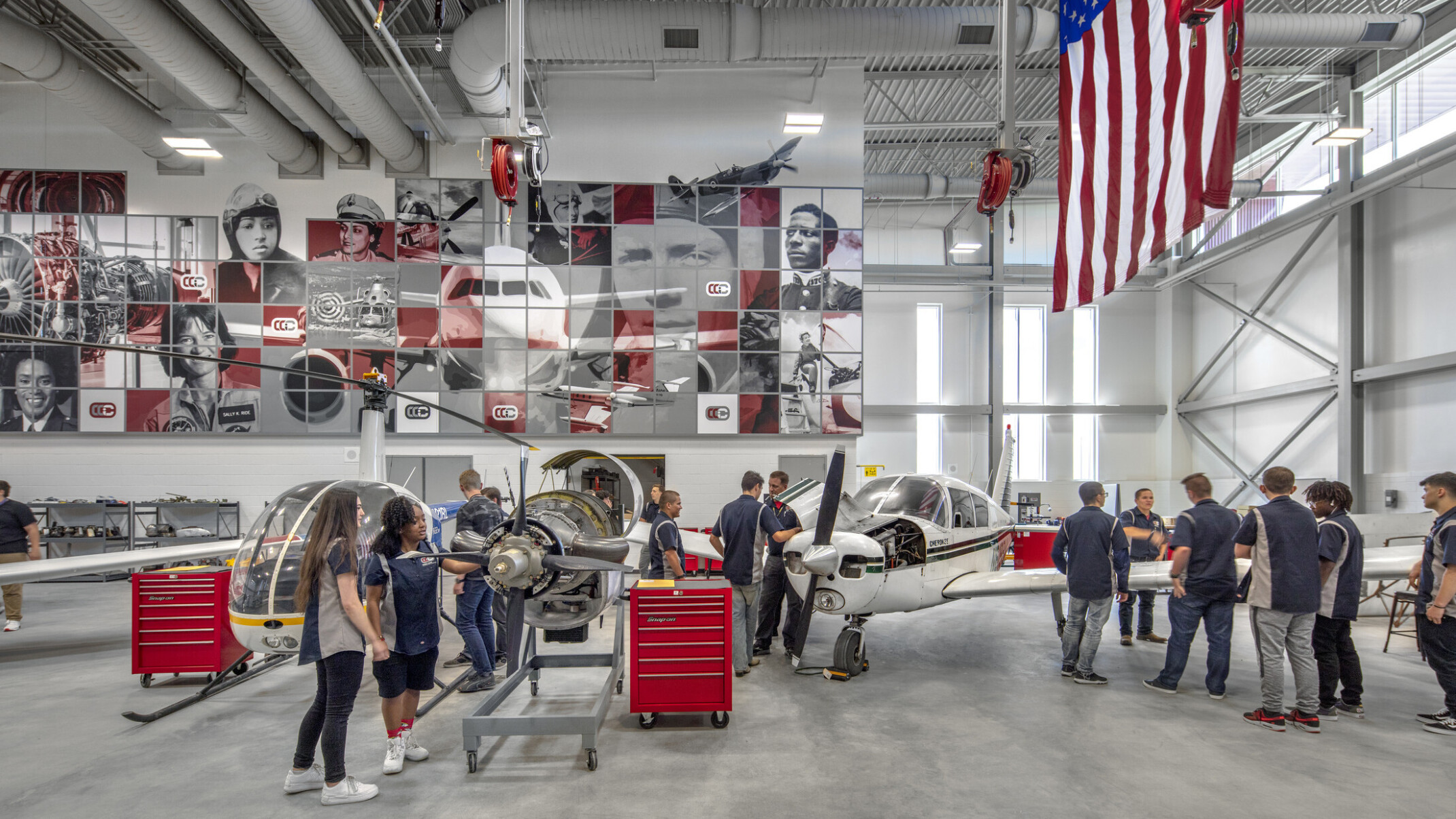 Aviation lab with helicopter, small plane, and displayed engine, mural at back with planes and pilots, american flag, right