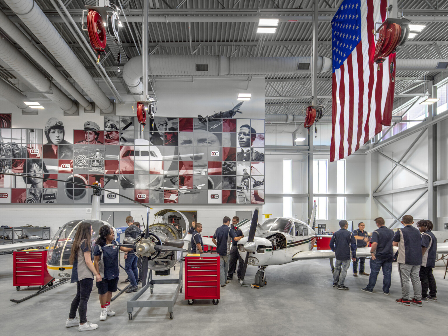 Aviation lab with helicopter, small plane, and displayed engine, mural at back with planes and pilots, american flag, right