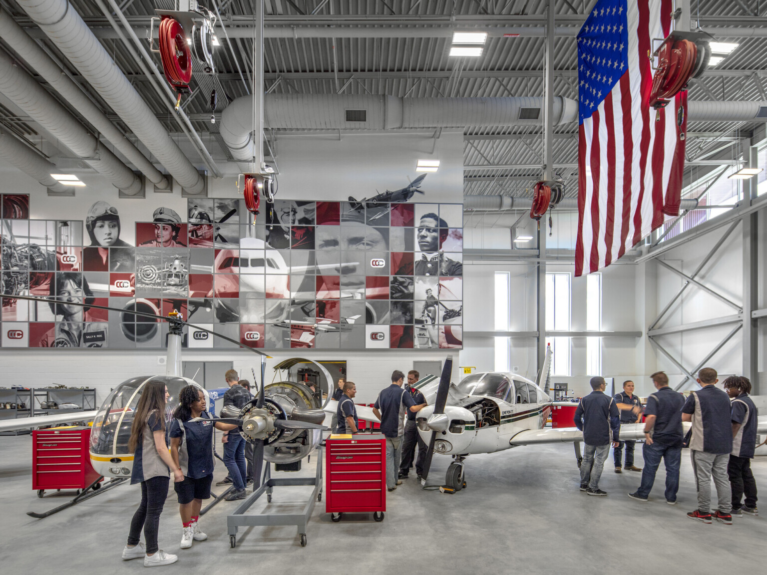 Aviation lab with helicopter, small plane, and displayed engine, mural at back with planes and pilots, american flag, right