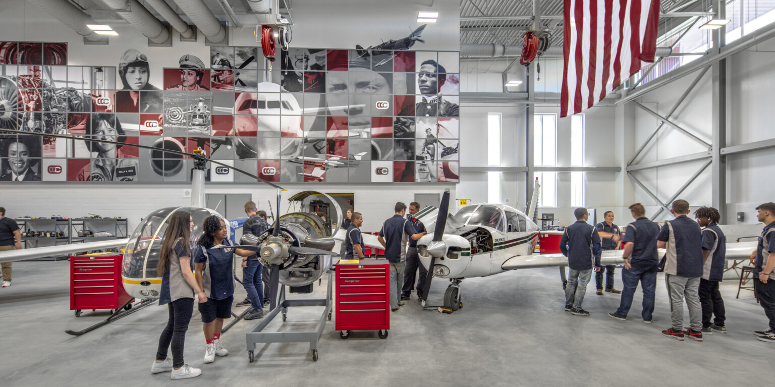 Aviation lab with helicopter, small plane, and displayed engine, mural at back with planes and pilots, american flag, right