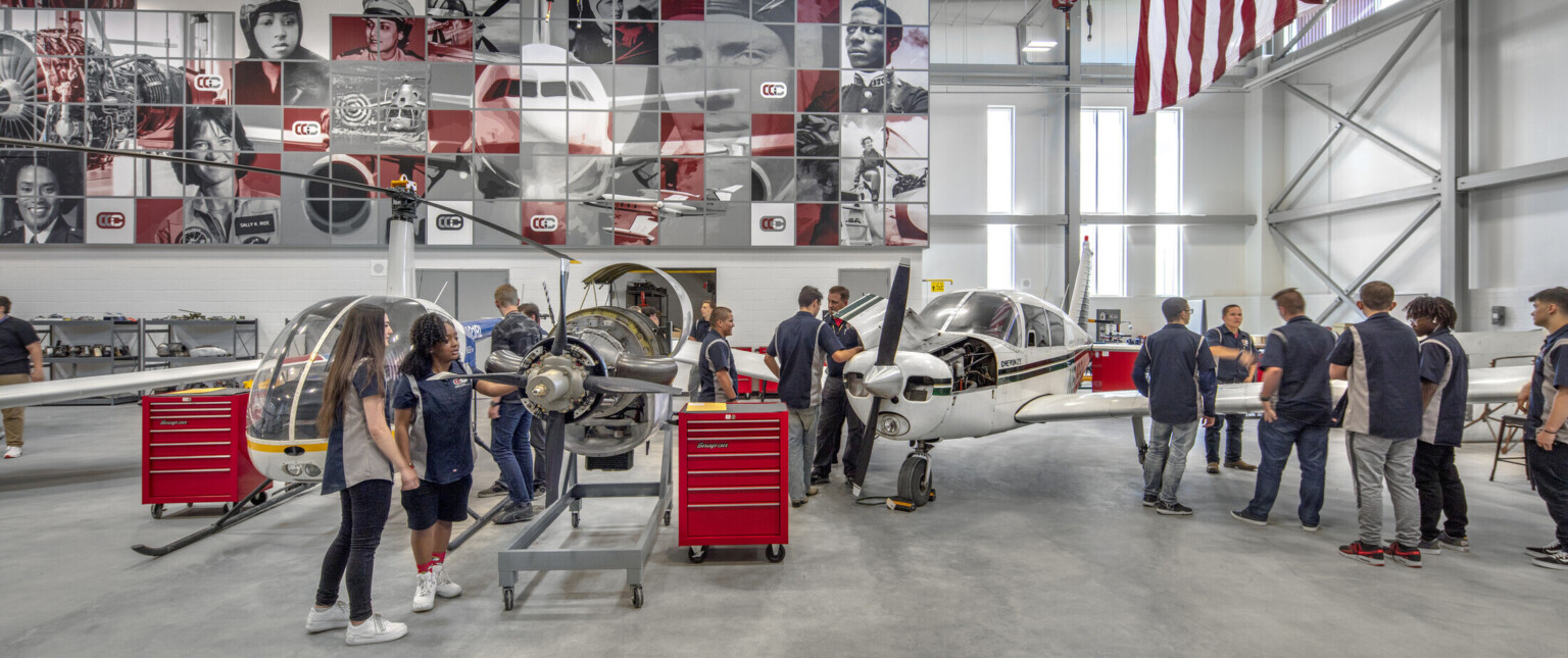 Aviation lab with helicopter, small plane, and displayed engine, mural at back with planes and pilots, american flag, right