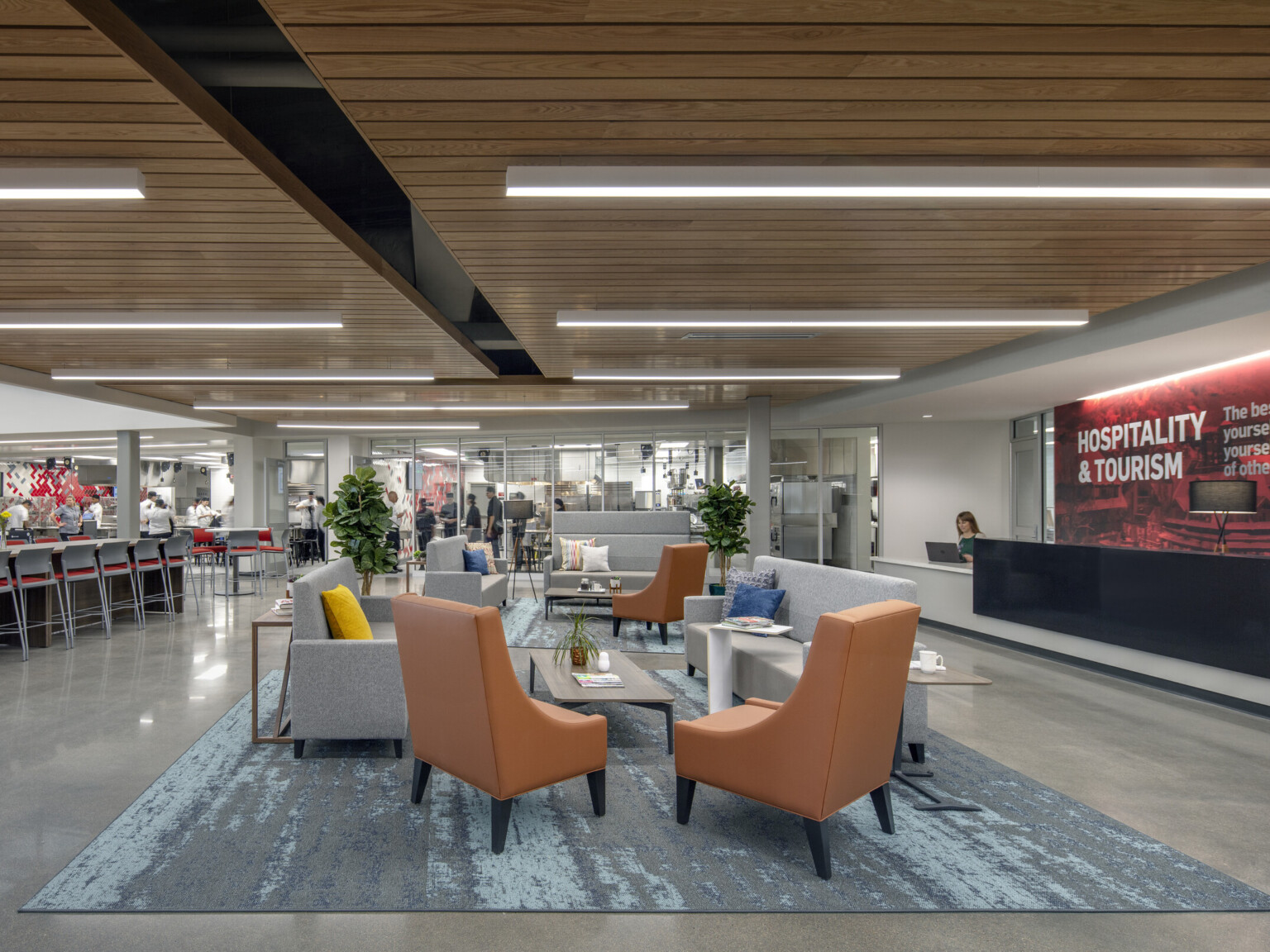 Seating area on blue carpet under wood panel drop ceiling details with the Hospitality and Tourism desk to the right