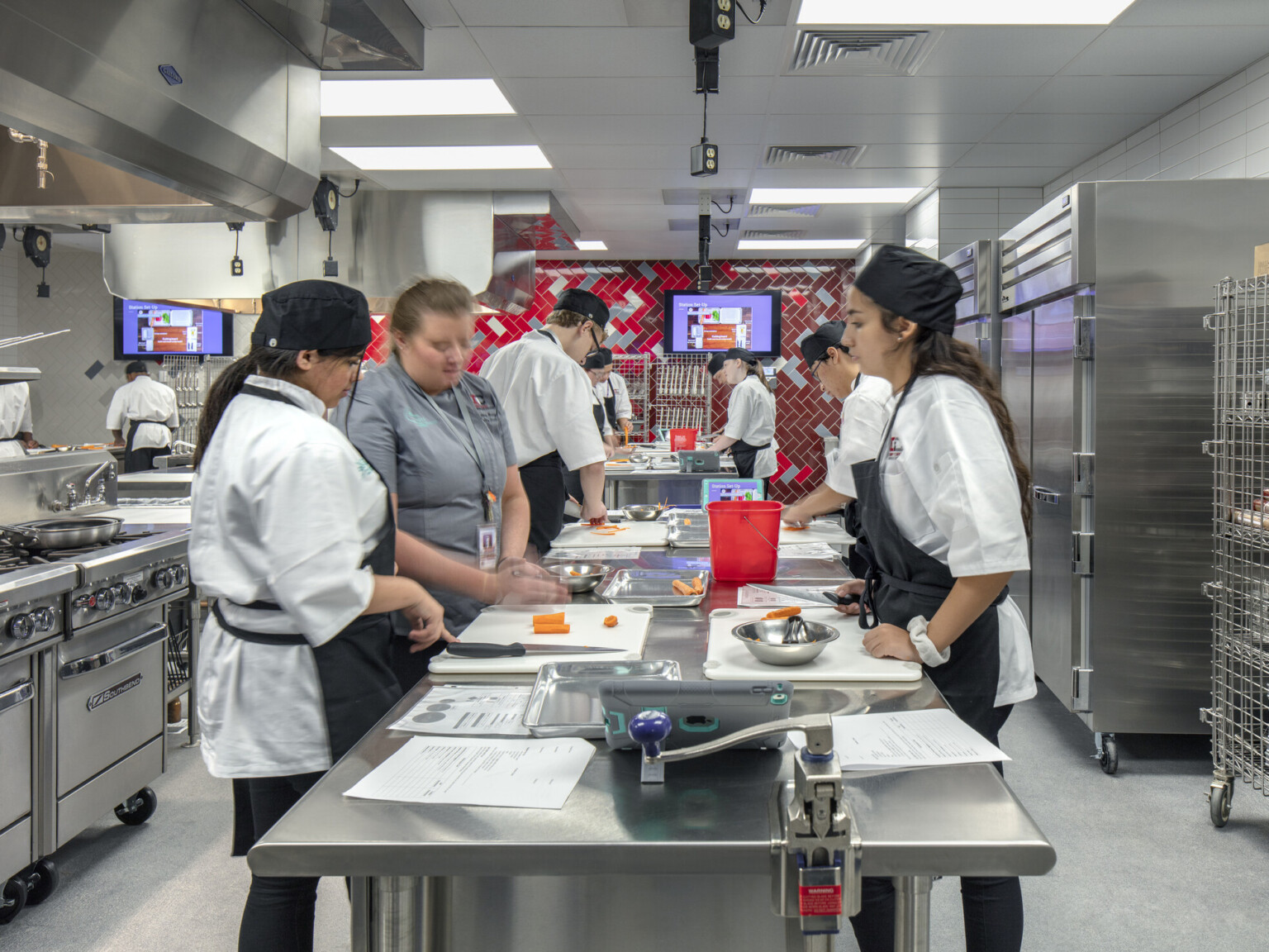 Culinary kitchen classroom with stainless steel island and red tile back wall. Stoves on left wall, refrigerators to right, cherry creek innovation campus, ccic cherry creek, cherry creek high school