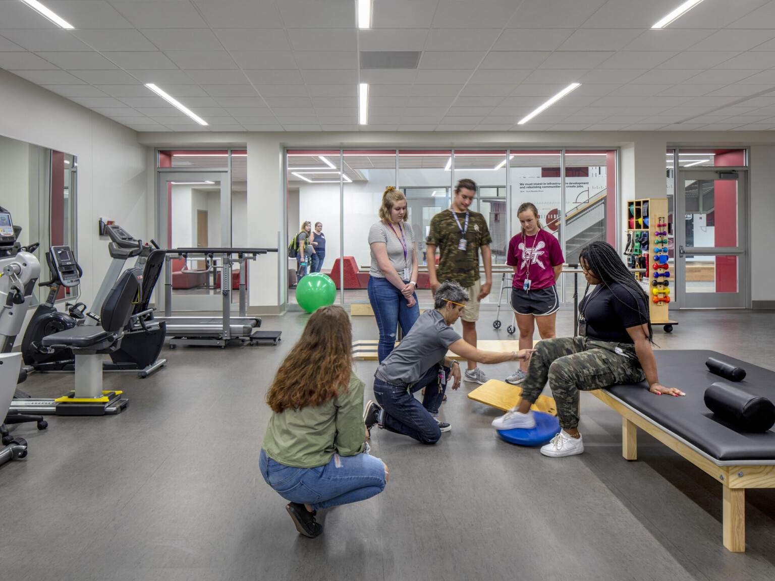 Classroom with cardio equipment to left wall facing mirror. Floor to ceiling windows, back, to hallway. Padded bench, center