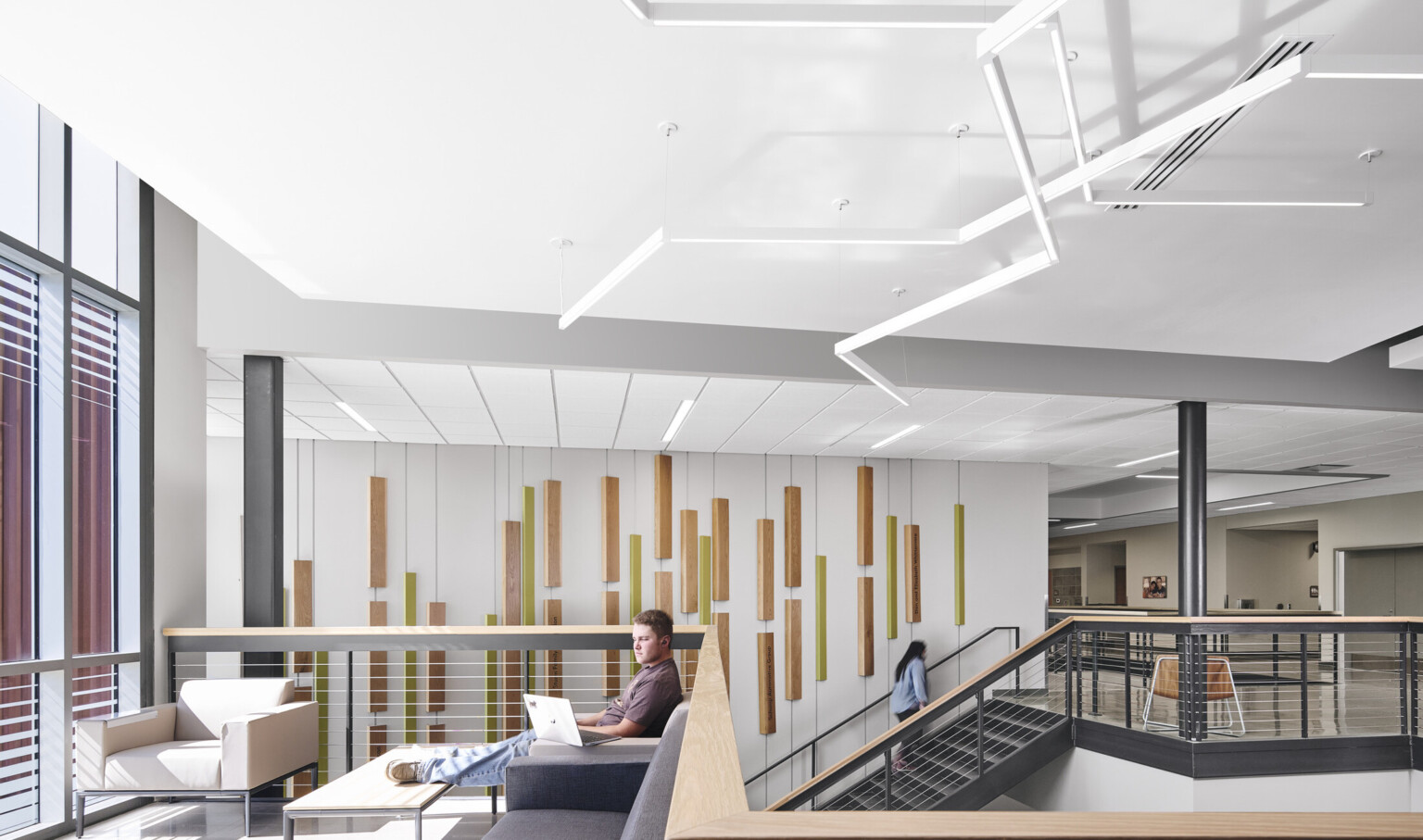 Entry separates red siding section of building, left, from right section with double height windows, white walls, modern, sculptured, abstract, tube lighting overhead, open stairway