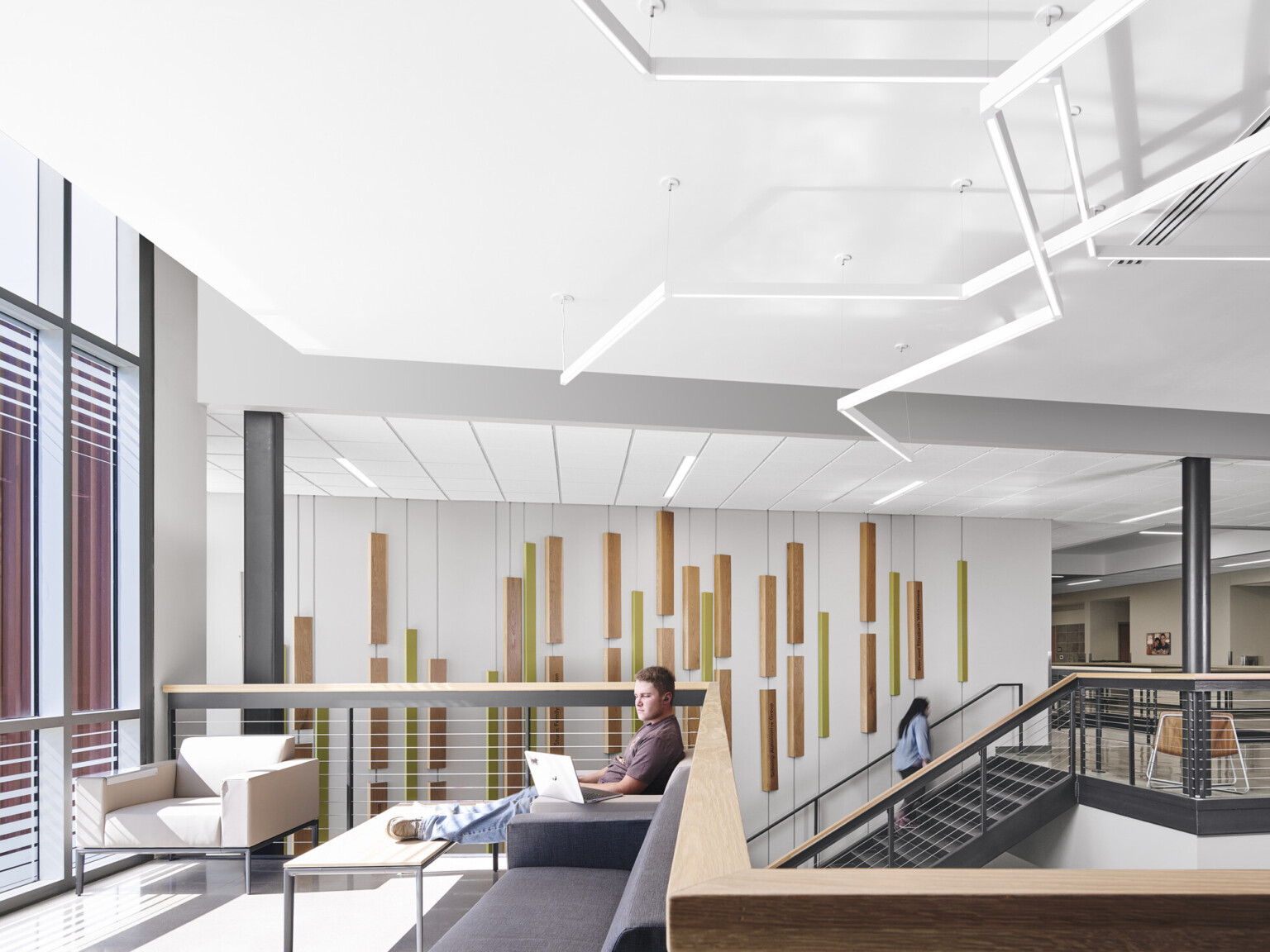 Entry separates red siding section of building, left, from right section with double height windows, white walls, modern, sculptured, abstract, tube lighting overhead, open stairway