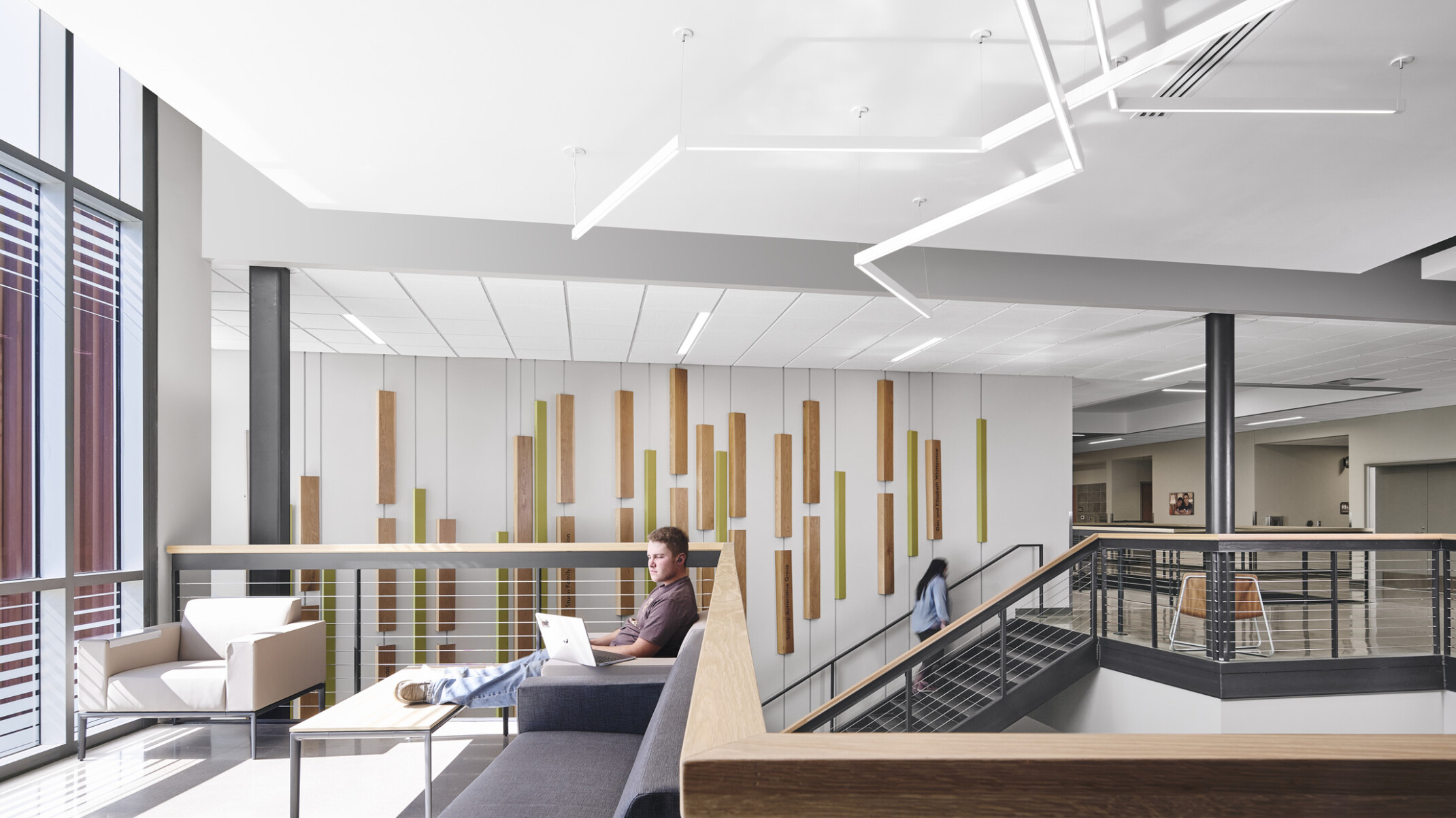 Entry separates red siding section of building, left, from right section with double height windows, white walls, modern, sculptured, abstract, tube lighting overhead, open stairway
