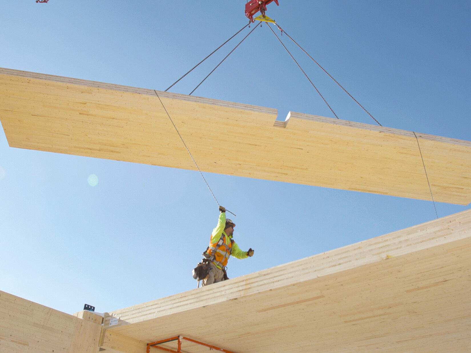 timber panel being lifted on a crane with construction worker directing