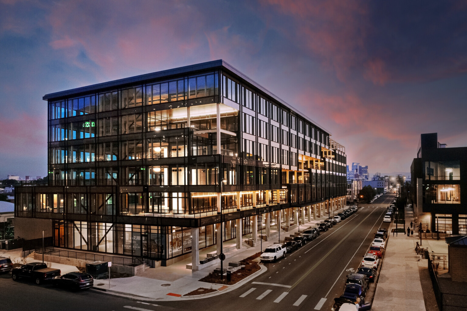 Industrial Mass Timber building at sunset; full floor to ceiling glass windows on every floor surrounded by structural elements; pedestrian walking space below Industrial Mass Timber building at sunset; full floor to ceiling glass windows on every floor surrounded by structural elements; pedestrian walking space below
