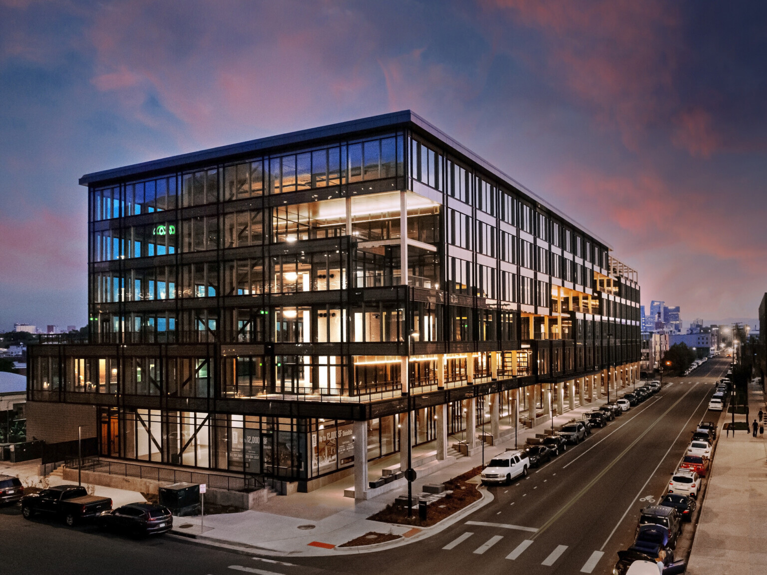 Industrial Mass Timber building at sunset; full floor to ceiling glass windows on every floor surrounded by structural elements; pedestrian walking space below