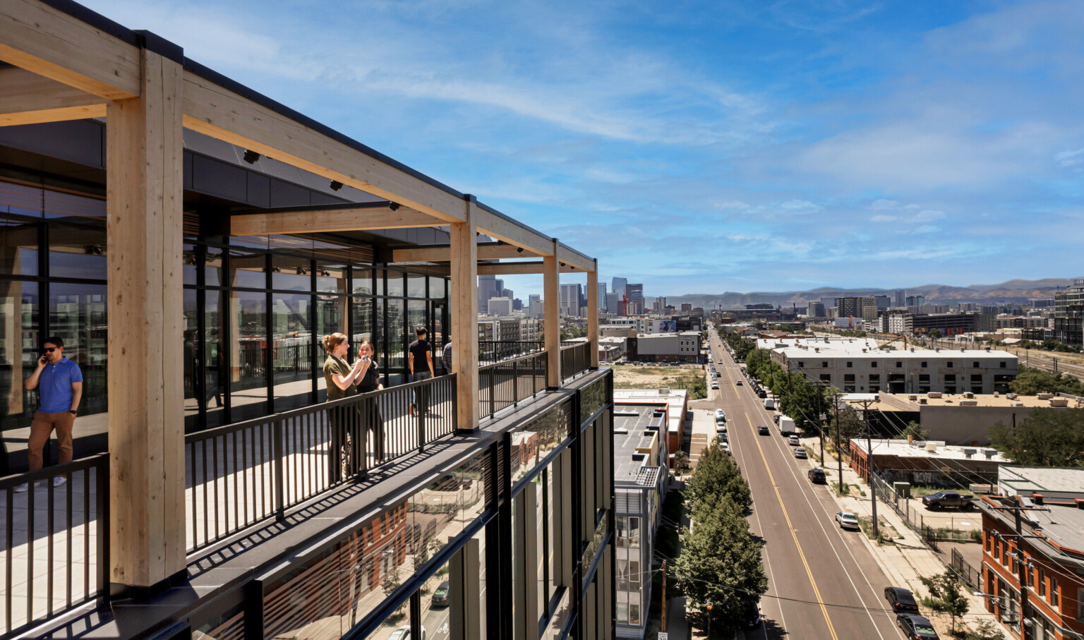 patio of a mass timber workplace and retail building overlooking the street and flat distant landscape; people on the patio looking out to the right views; on the phone; mass timber beams exposed