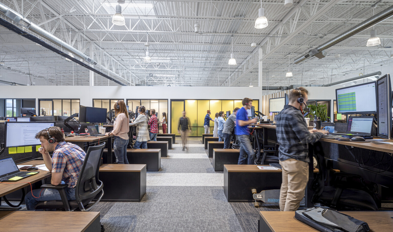 2 rows of opposite facing adjustable height desks in double height room in front of wall with translucent yellow windows