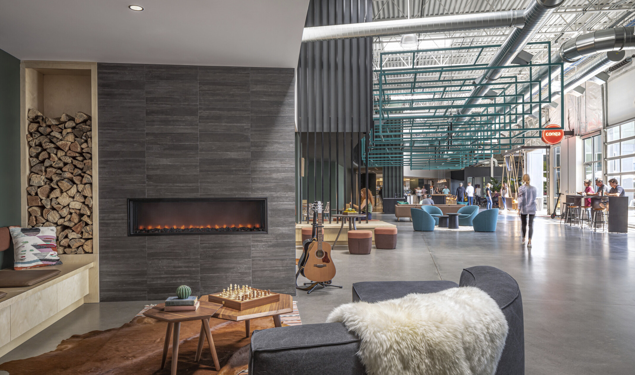 Conga Headquarters seating area with garage door windows on right wall. Couch at front left in front of fireplace