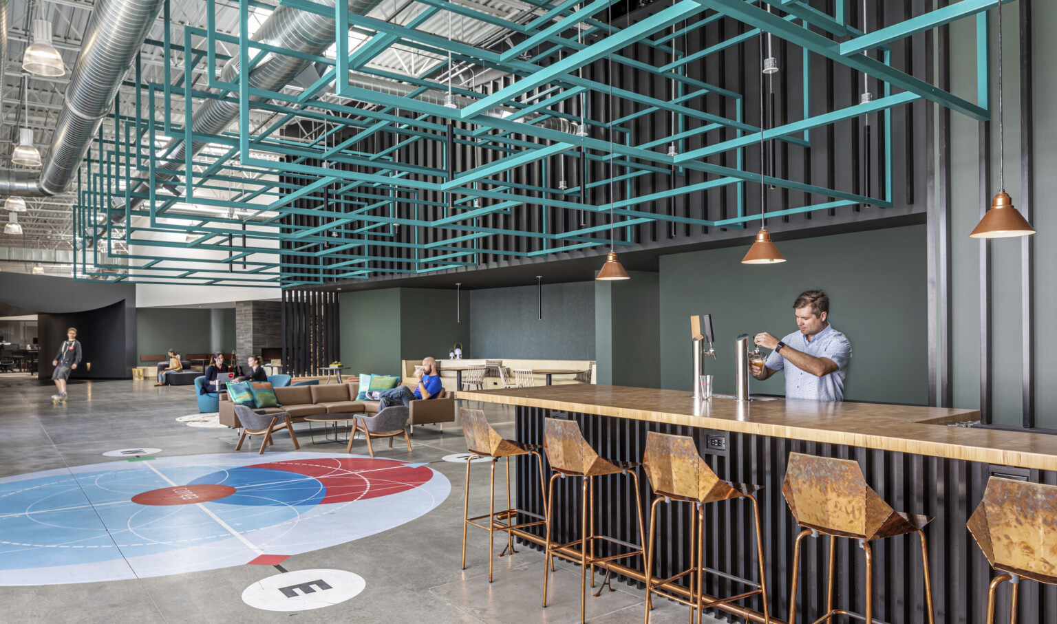 Counter with beer taps in large double height hallway lined with seating. Above, blue metal angular sculpture hangs