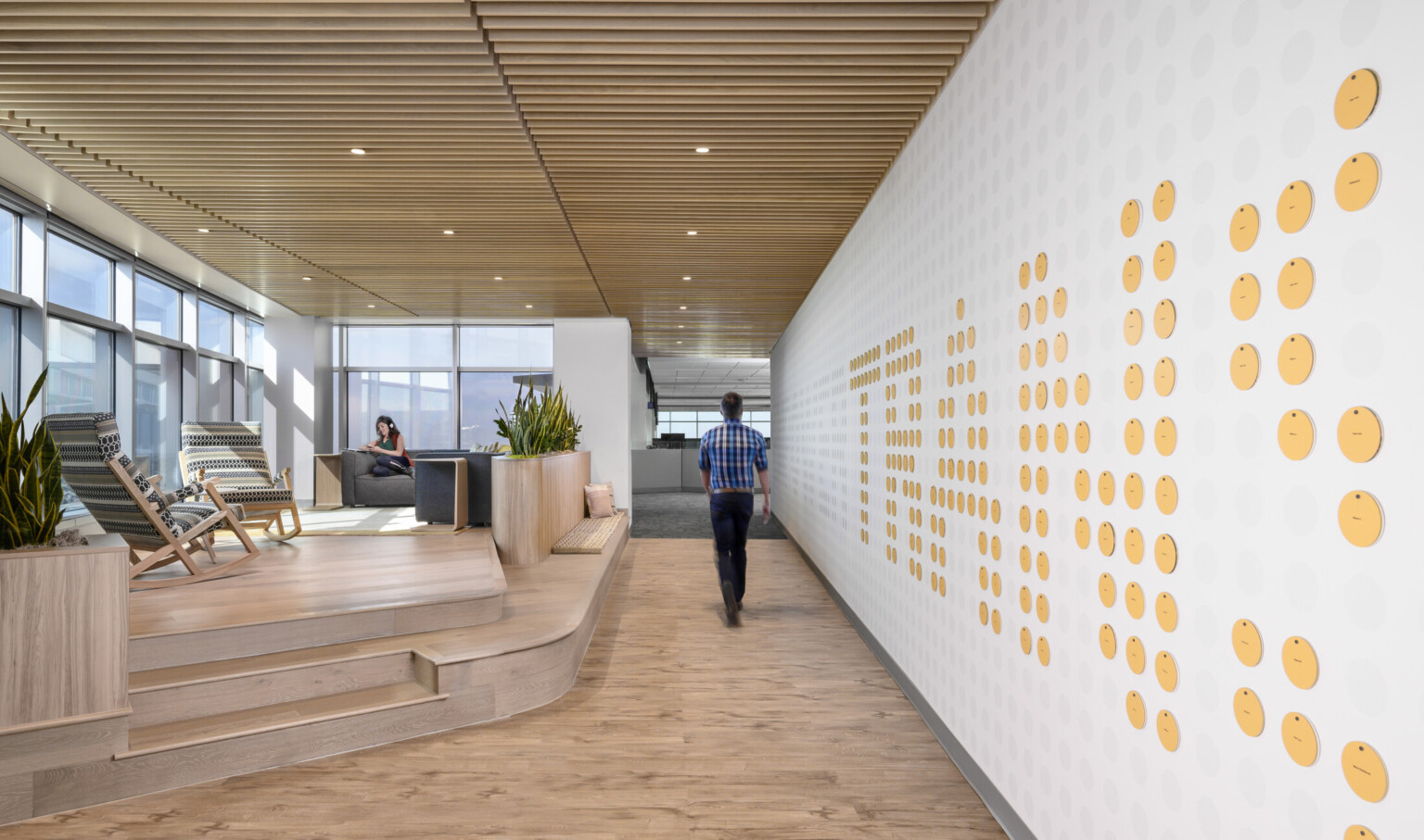 Wood slat ceiling over hallway, mezzanine with floor to ceiling windows and seating to left. Wall, right, with circle details