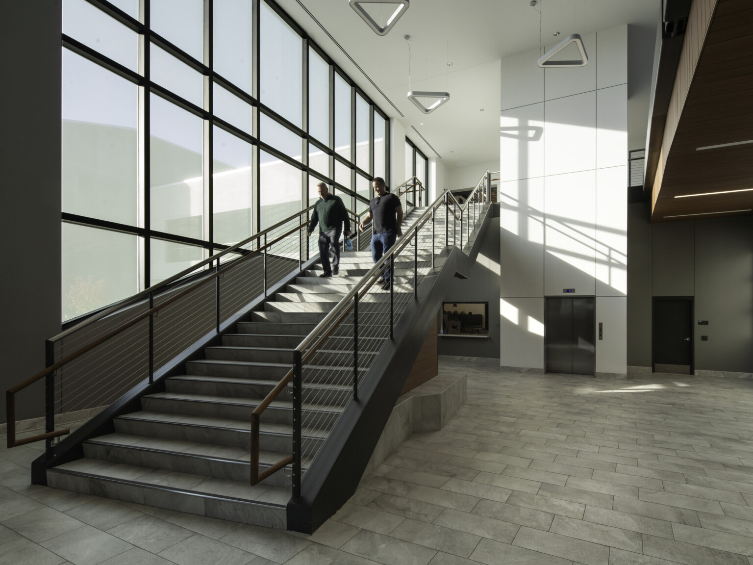 Interior stairway with modern lighting suspended from the ceiling looking at an elevator