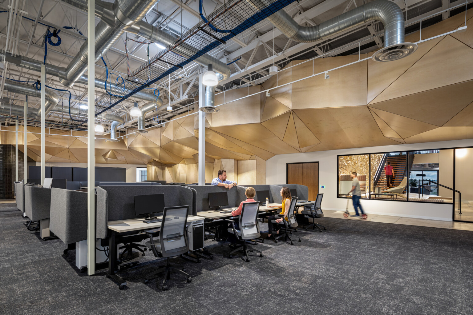 interior of a workplace with open desking, sculptural wood ceiling, and exposed ductwork