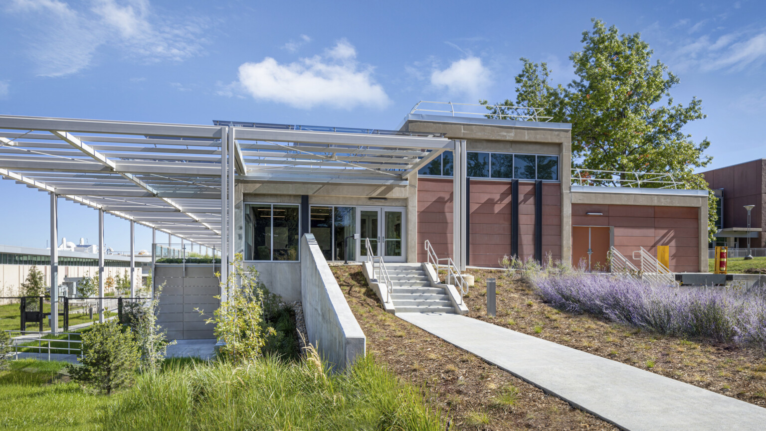 Multilevel building set into a hill with white awnings, stepped tiers and purple and green landscaping