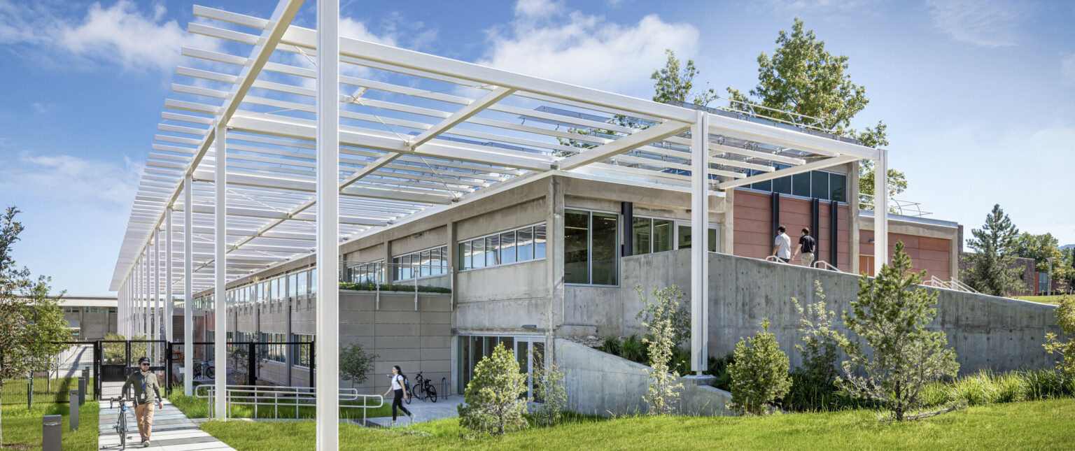 Modern multistory building built into a hill with white metal decorative columns and lush landscaping