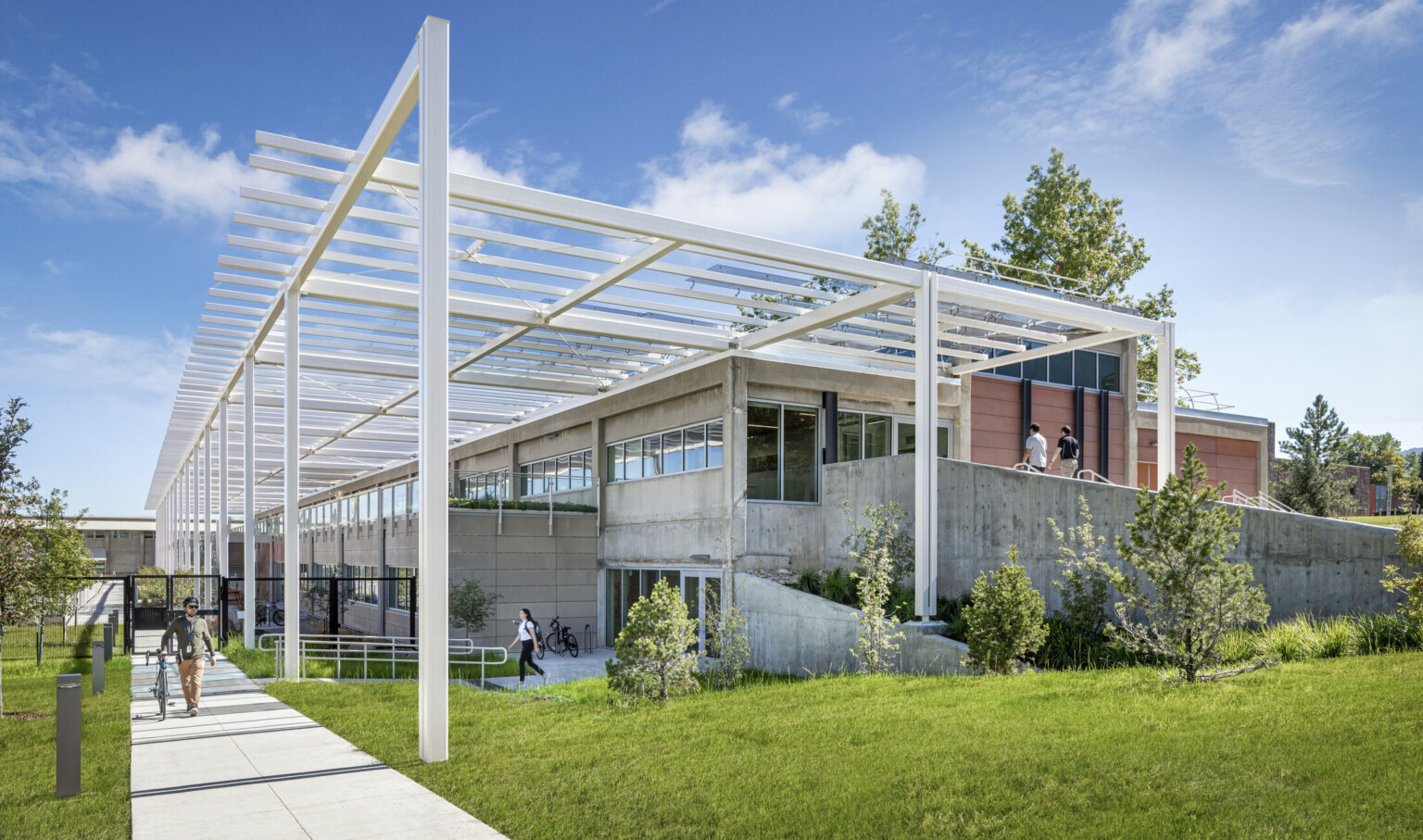 Modern multistory building built into a hill with white metal decorative columns and lush landscaping