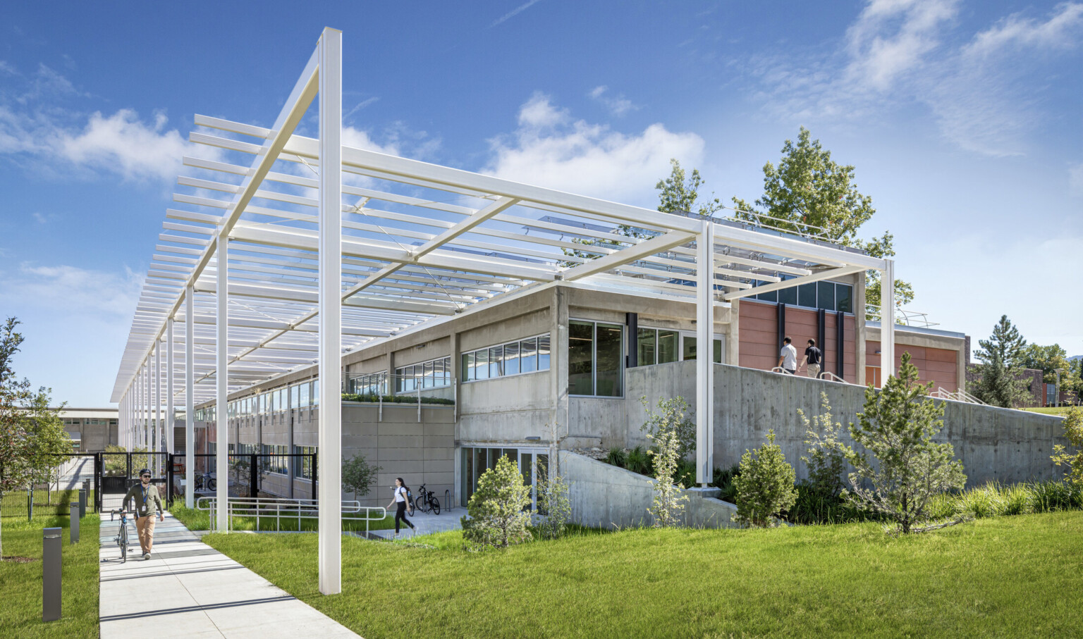 Modern multistory building built into a hill with white metal decorative columns and lush landscaping