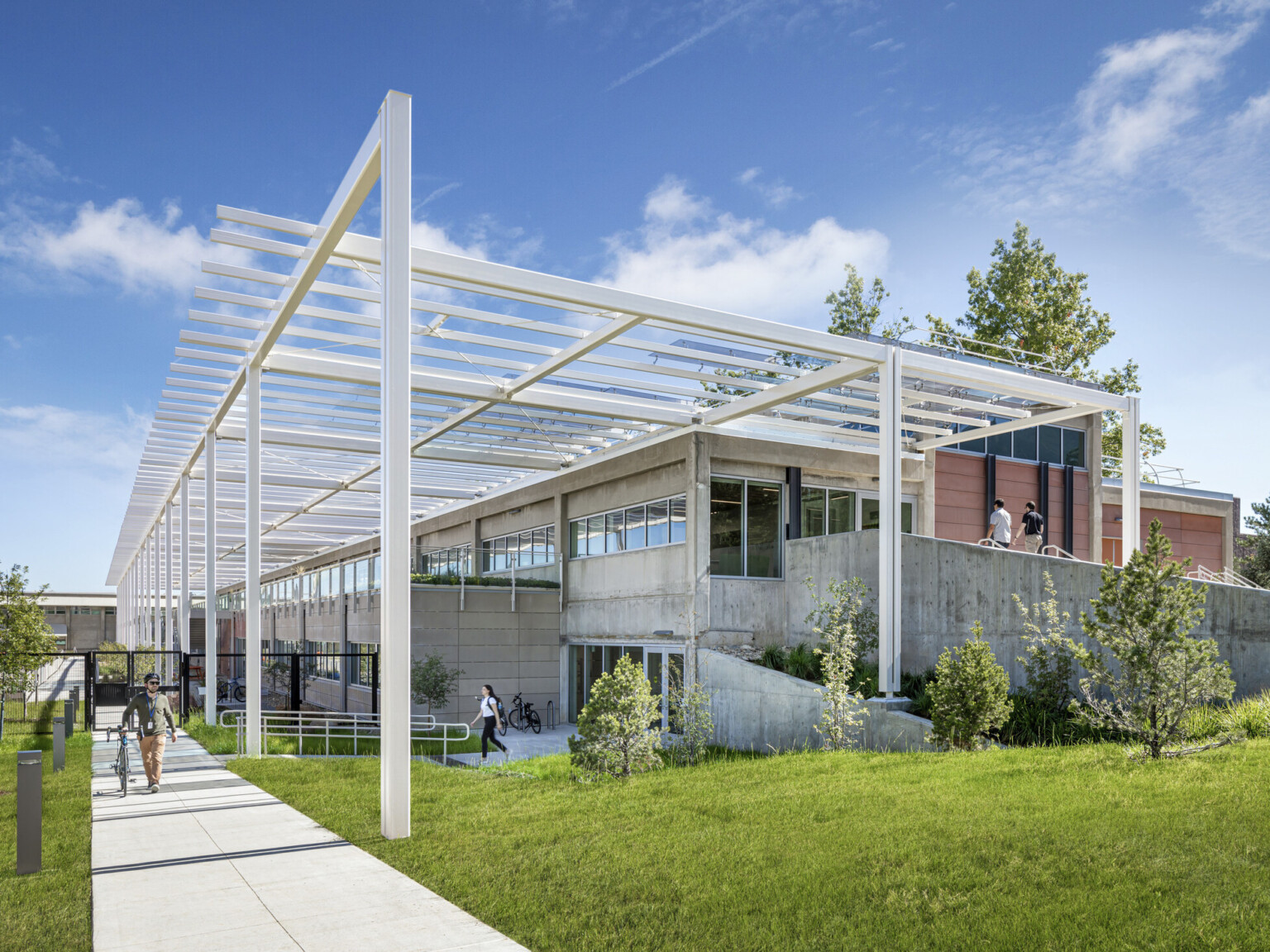 Modern multistory building built into a hill with white metal decorative columns and lush landscaping