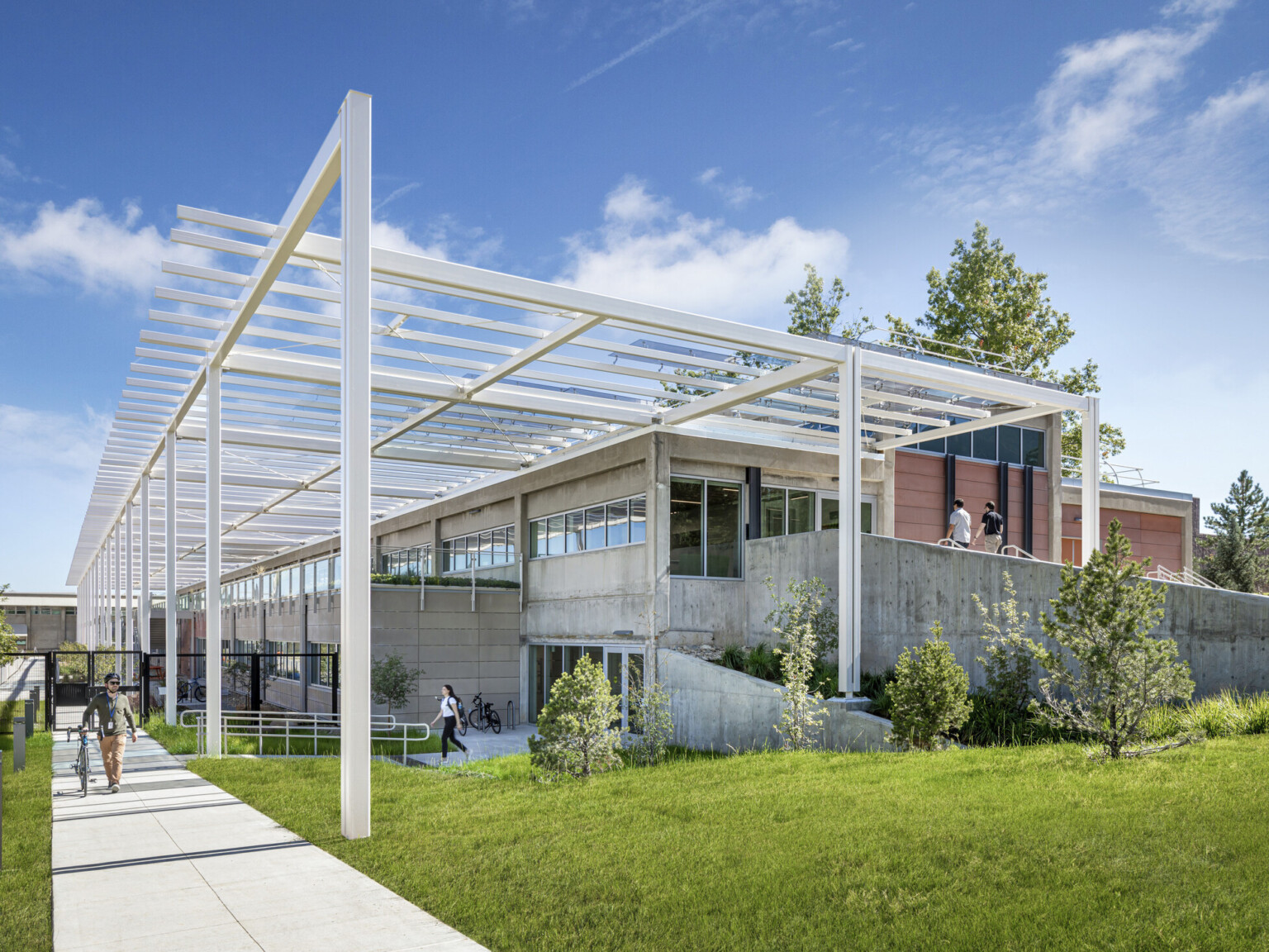 Modern multistory building built into a hill with white metal decorative columns and lush landscaping